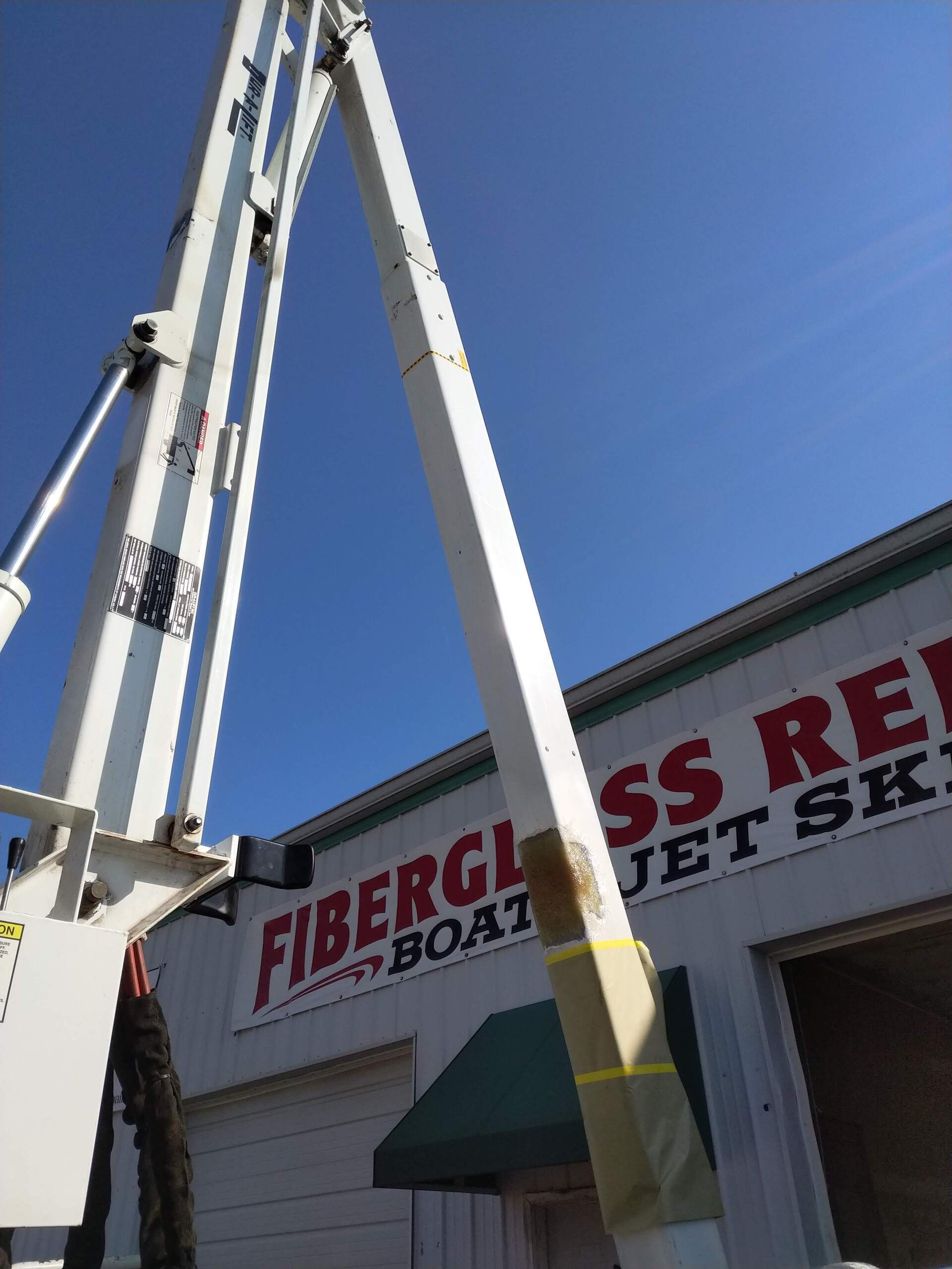 Tall white fire truck ladder beside a store sign reading “Fiberglass Repair” under a blue sky
