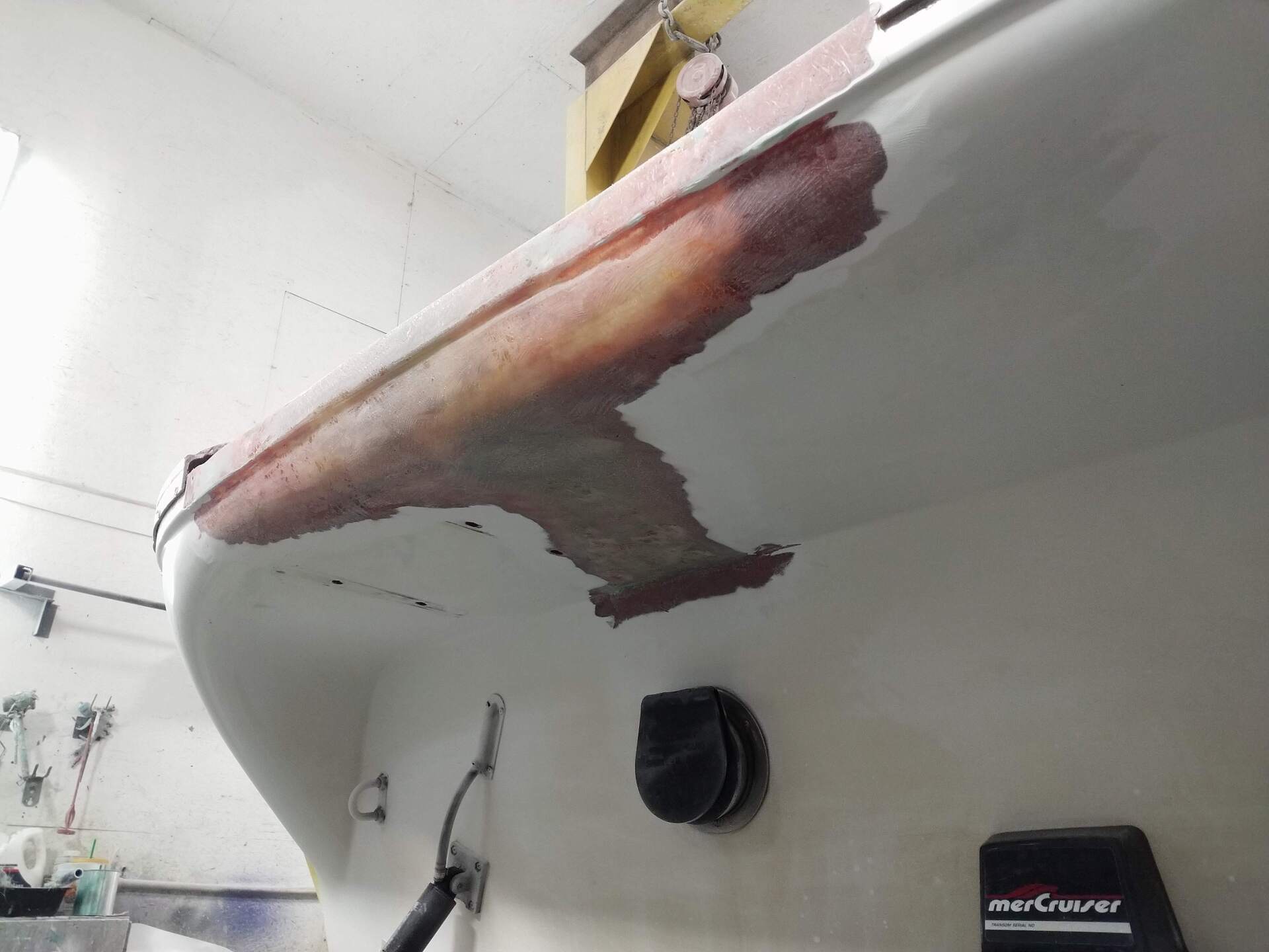 White boat hull in a workshop, with a large brown repair patch near the bow.