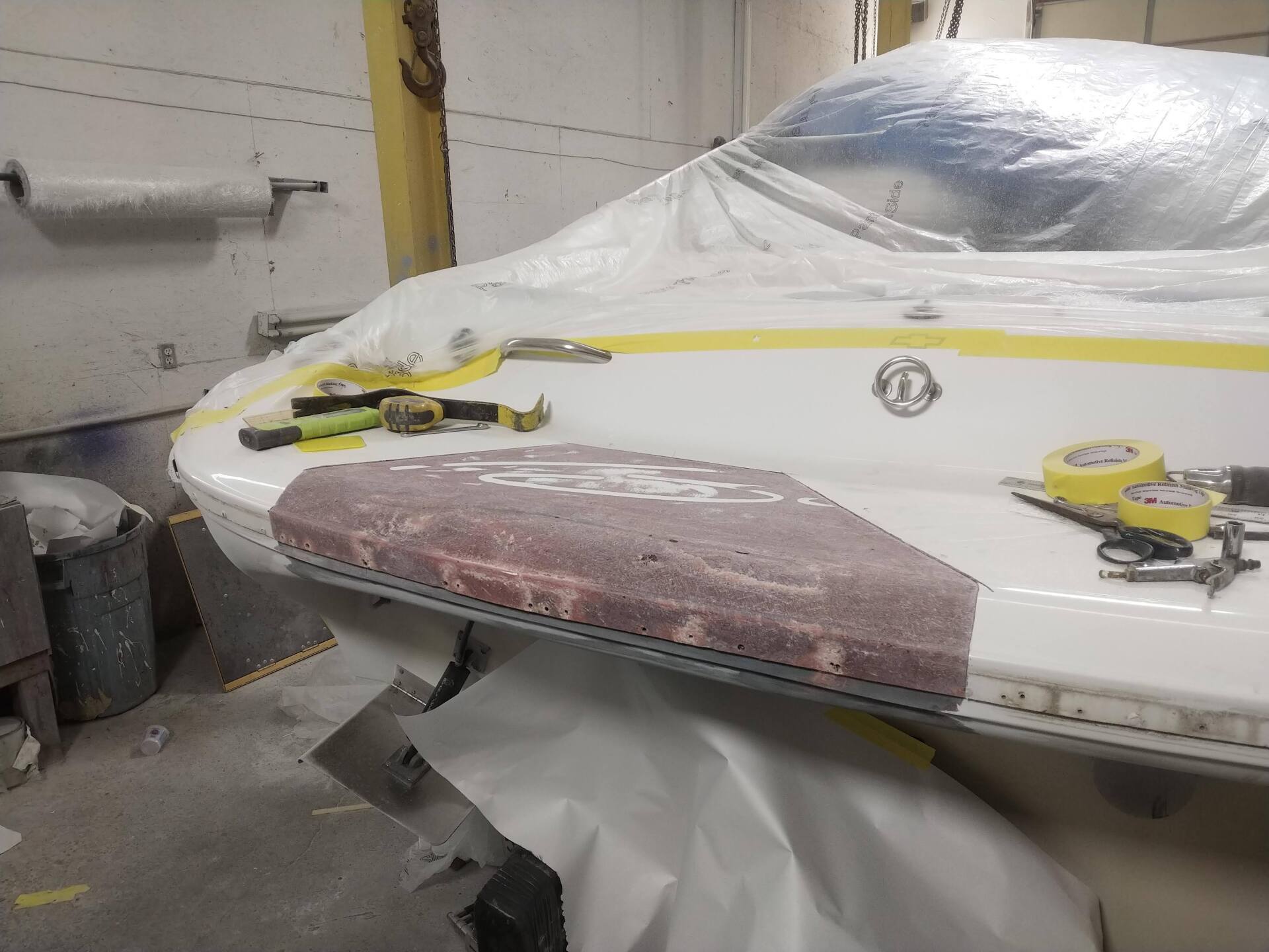 White boat hull in a workshop, covered with masking tape and sanding dust during repair.