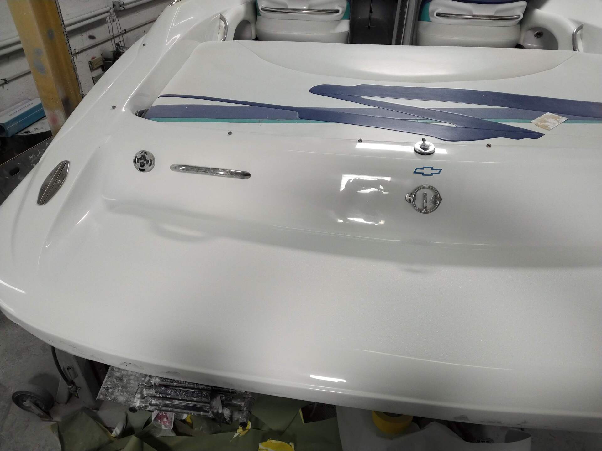 White boat bow with blue stripes in a workshop, showing a windshield and deck hardware