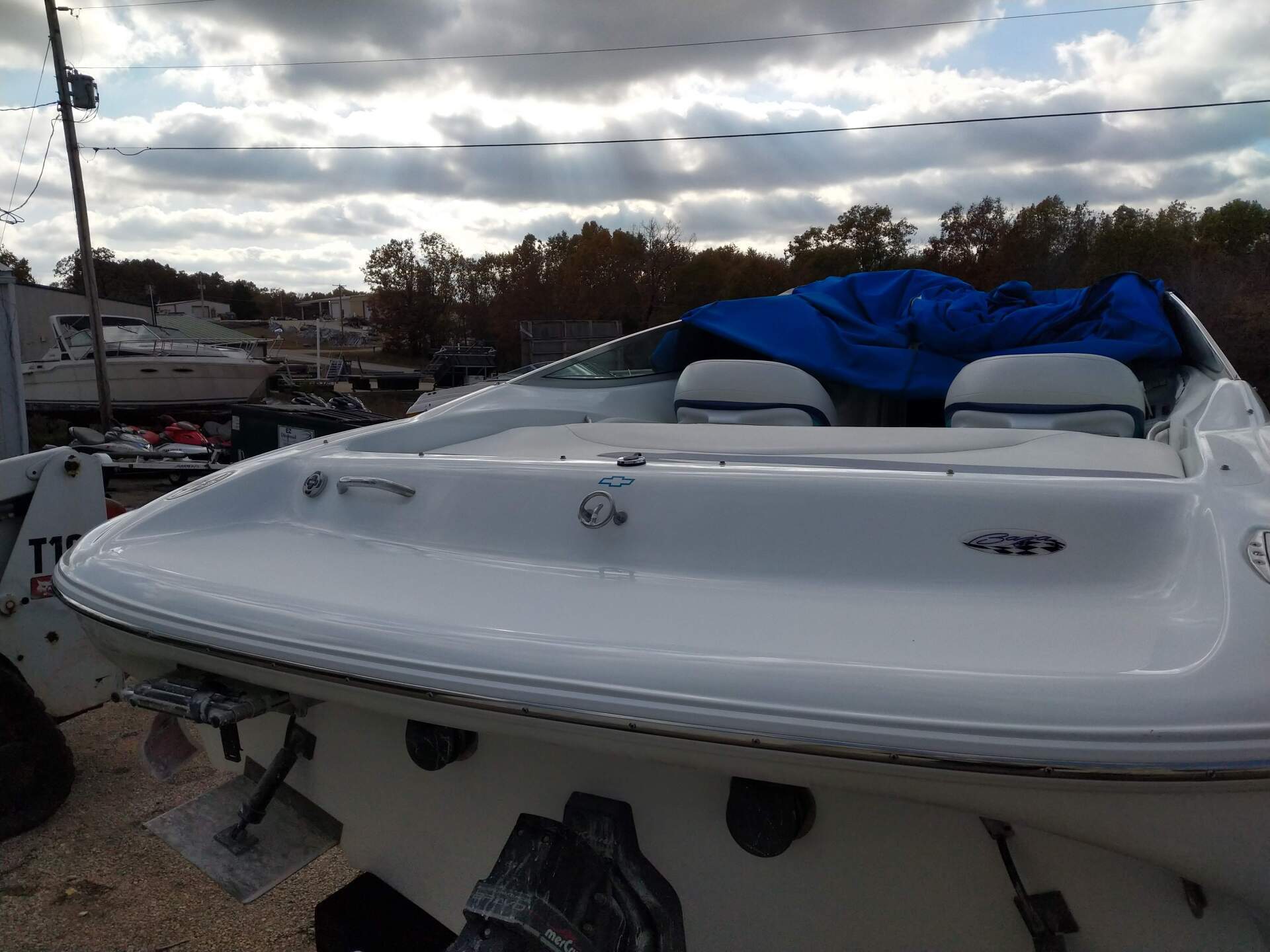 White boat on a trailer at a marina, covered with a blue tarp under a cloudy sky