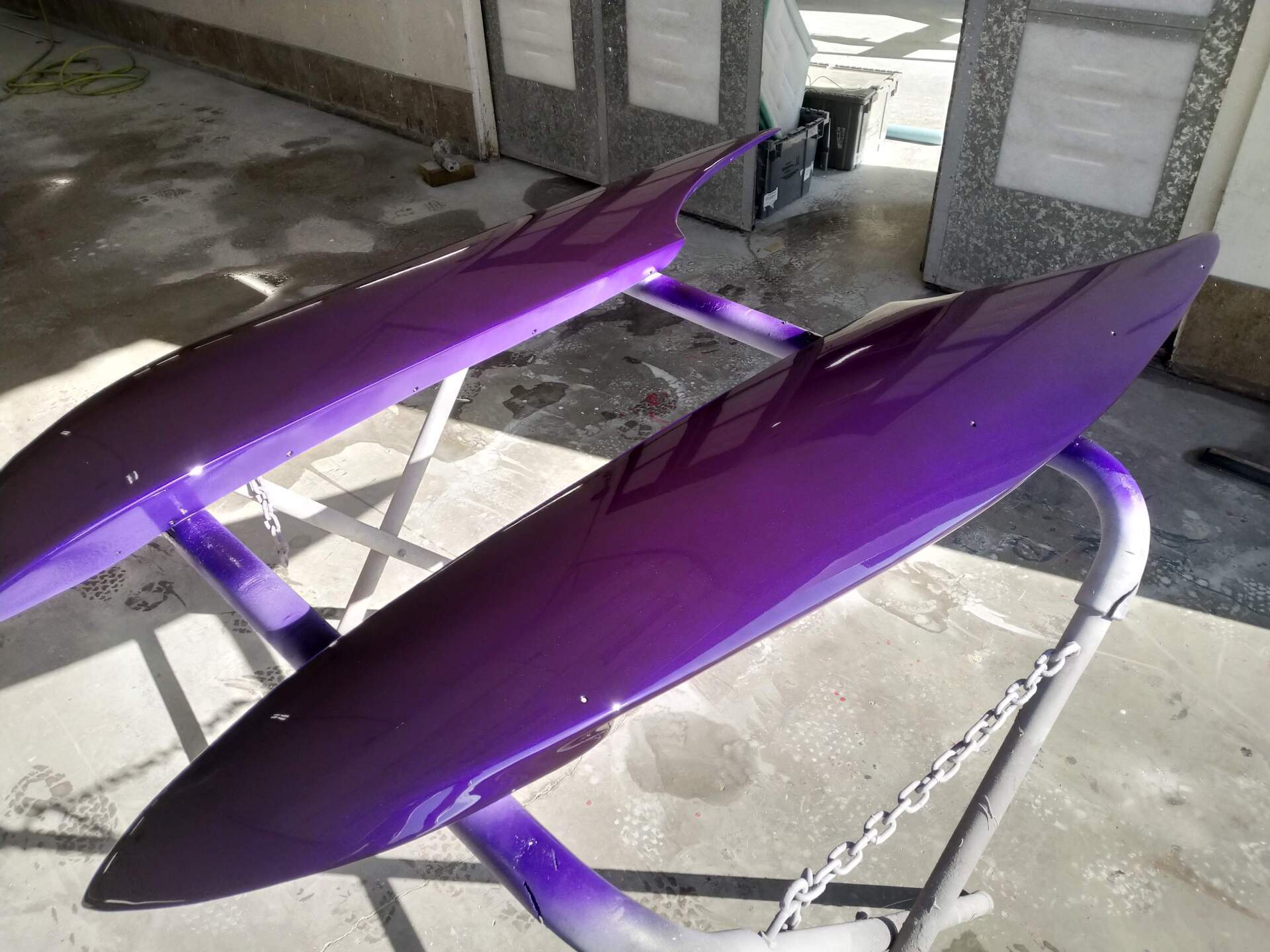 Purple kayak or canoe hull resting on a metal stand in a garage-like space.