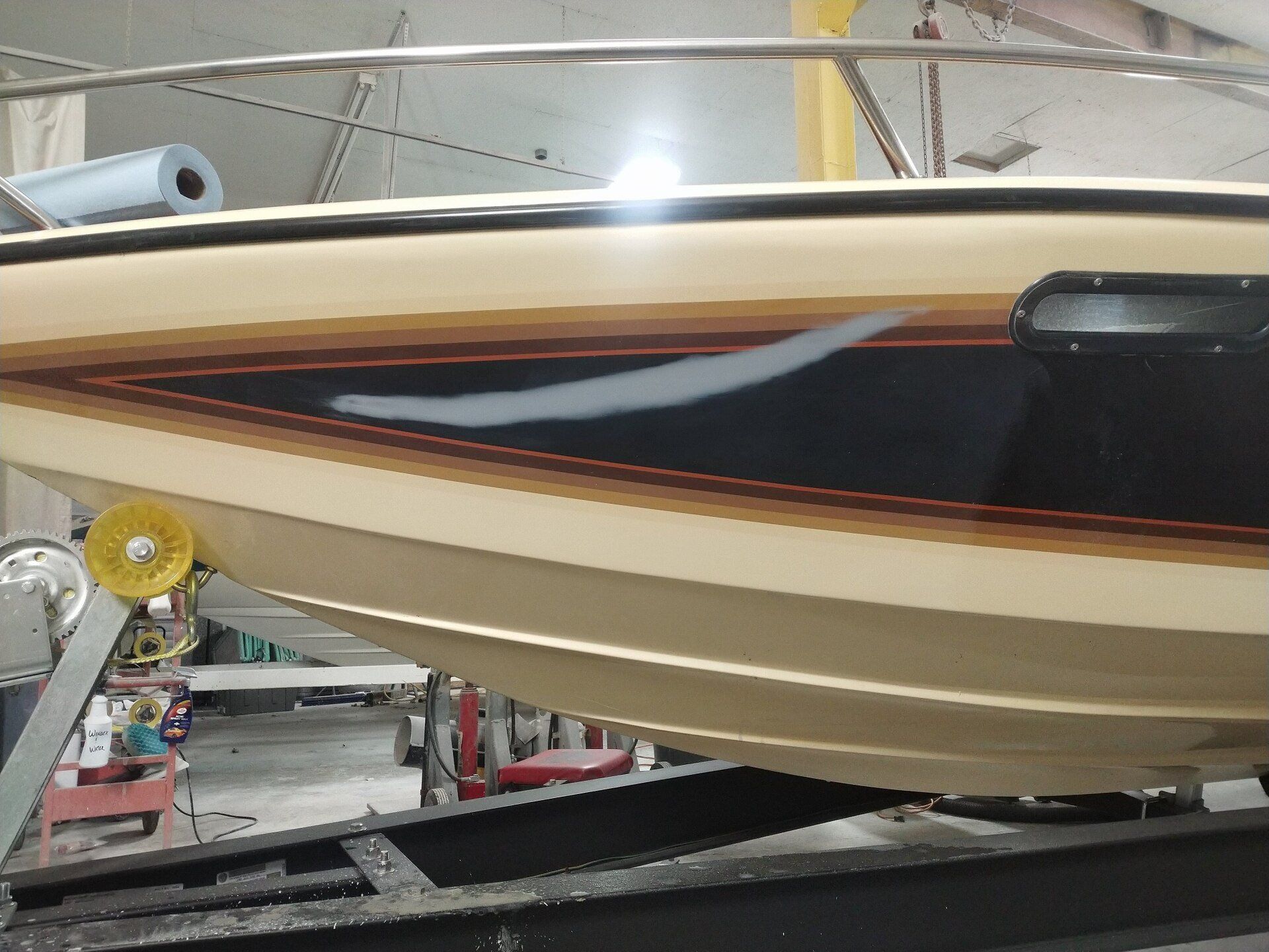 Cream and black speedboat hull on a trailer in a garage, with red and gold trim