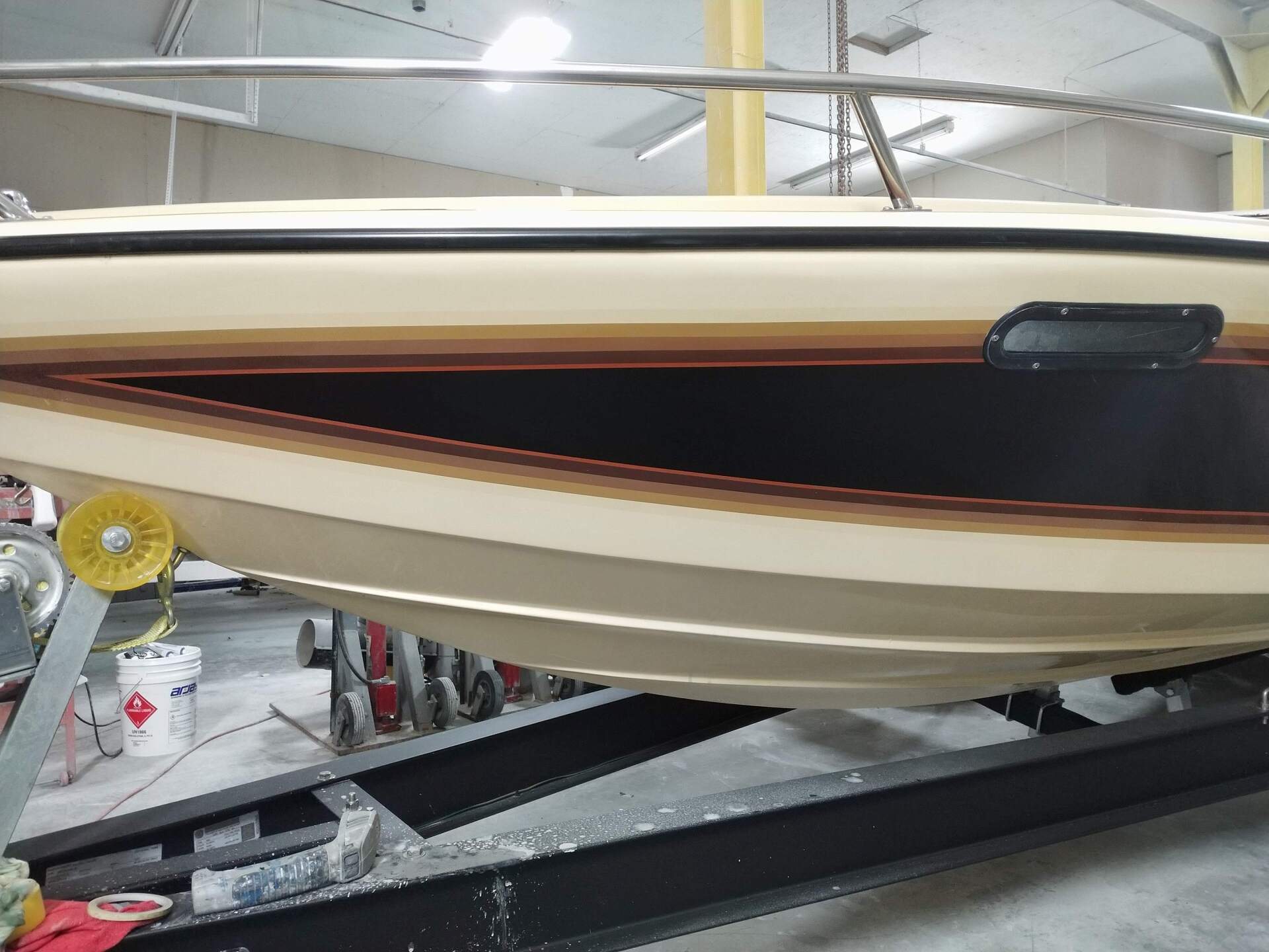 Cream and white motorboat on a trailer inside a workshop, with a dark tinted hull stripe.