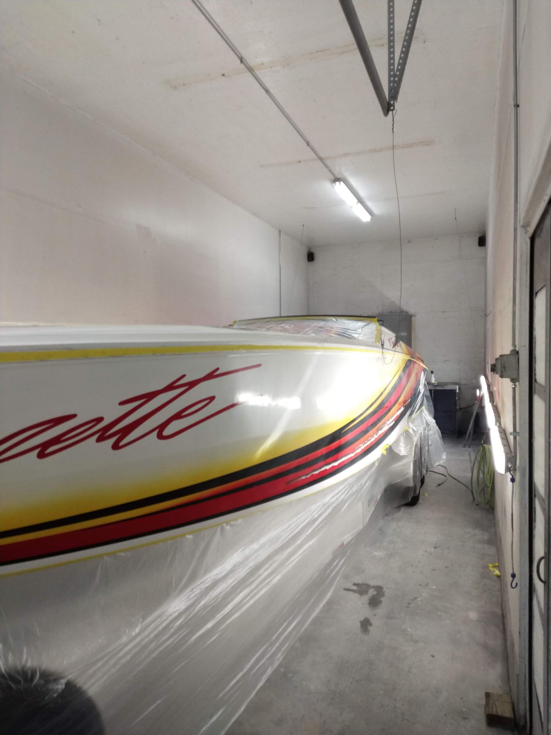 Covered speedboat in a narrow garage, with white hull and red-yellow stripes