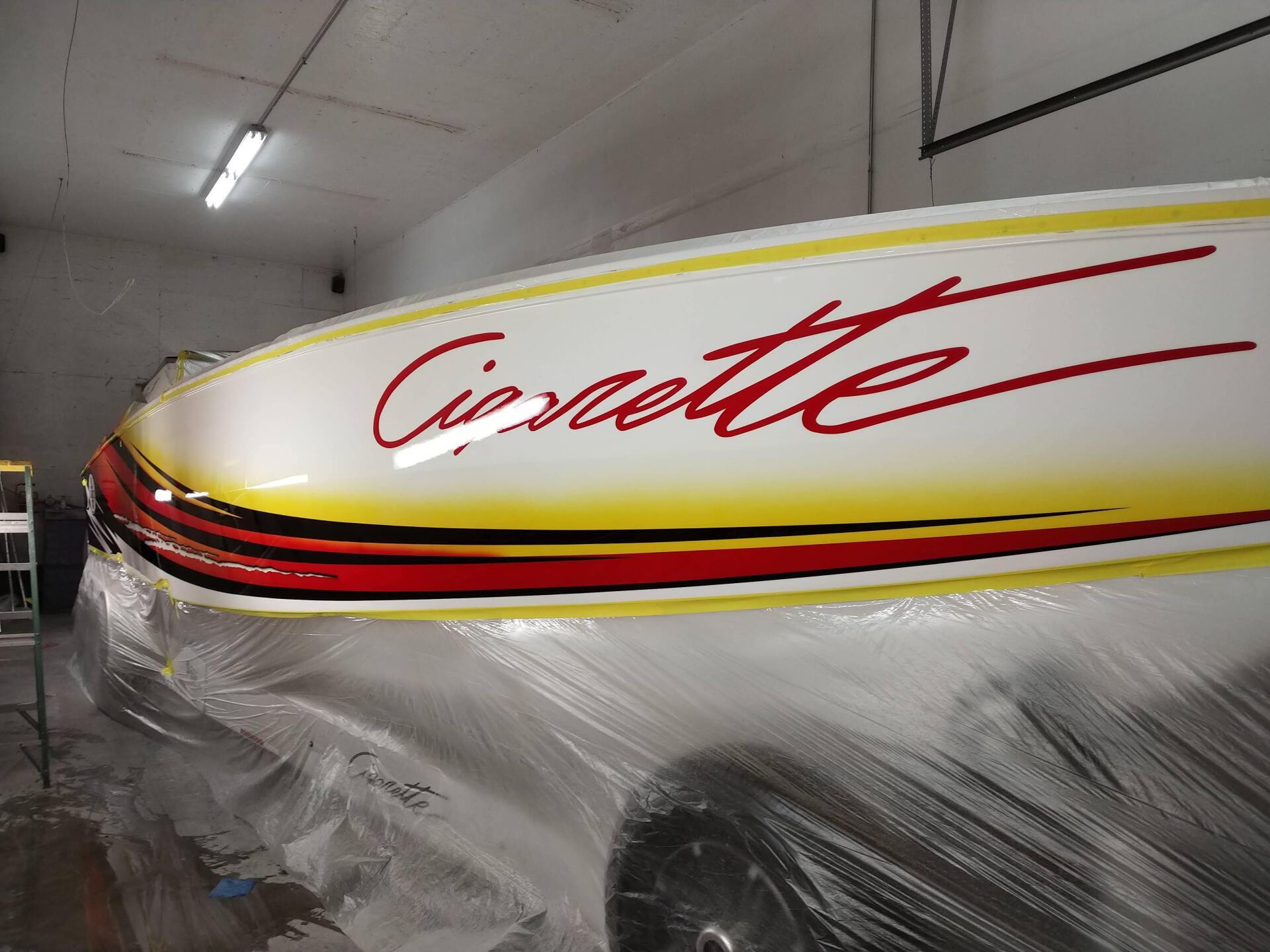 White boat with red “Cigarette” logo, wrapped in plastic inside a workshop
