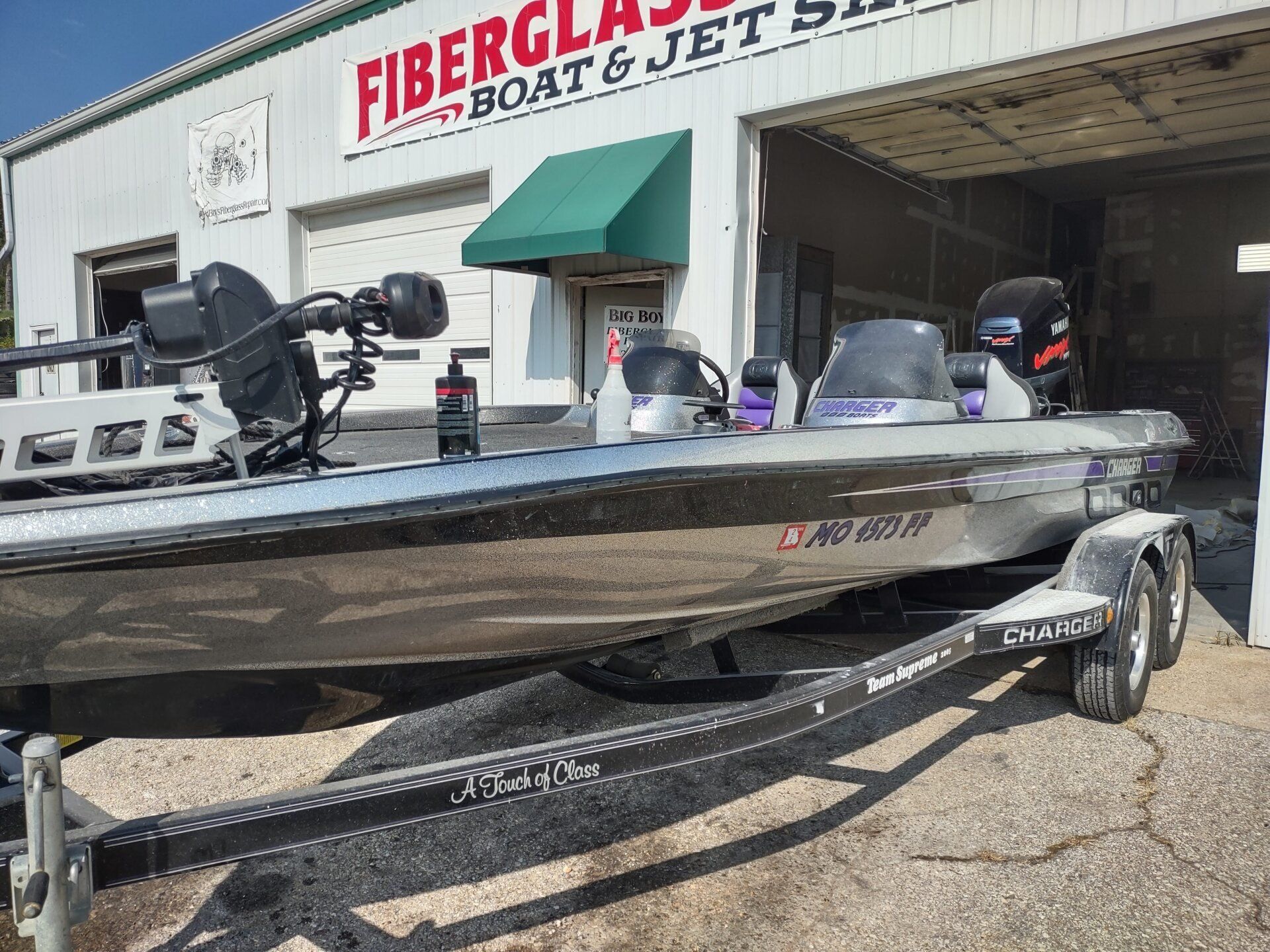 Three bass boats on trailers outside a fiberglass boat repair shop