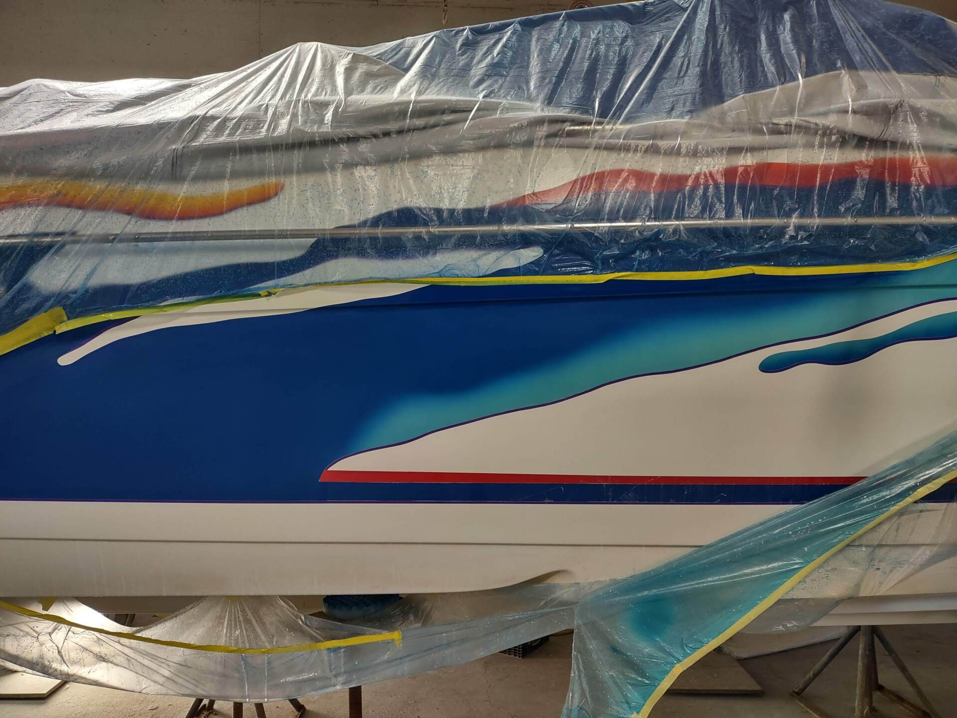 Covered boat hull with blue, white, and red paint under protective plastic tarp