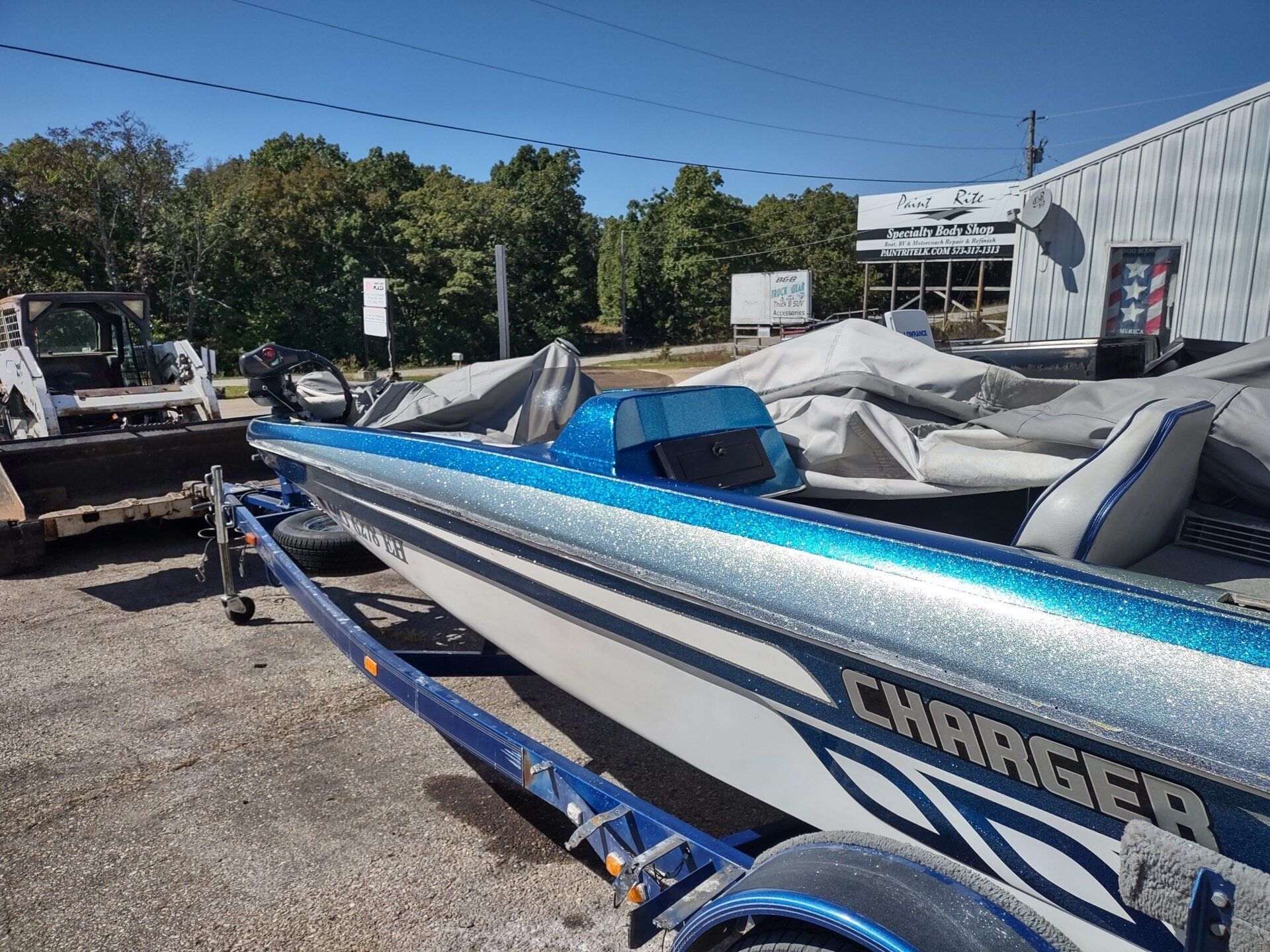 Blue-and-white Charger speedboat on a trailer in a boat yard, with covered boats and a truck nearby.