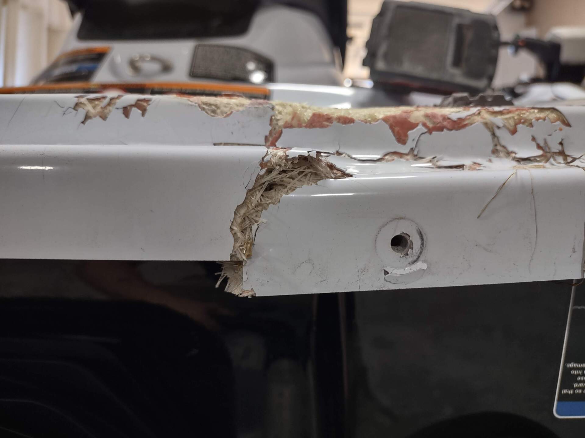 Close-up of a white vehicle’s damaged body panel with rust, chipped paint, and a dented hole