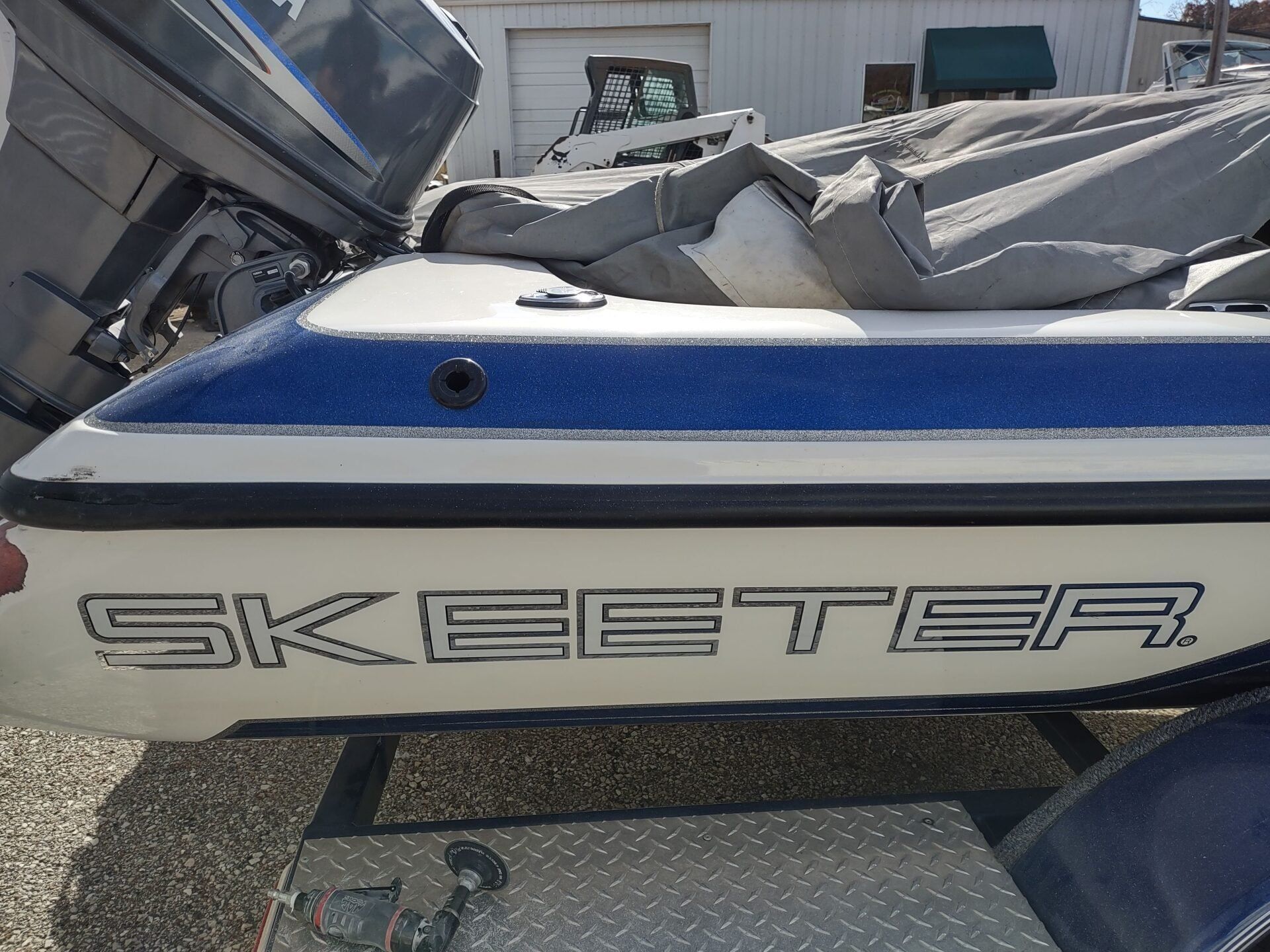 Blue and white Skeeter boat parked on a trailer with seats covered in gray tarps