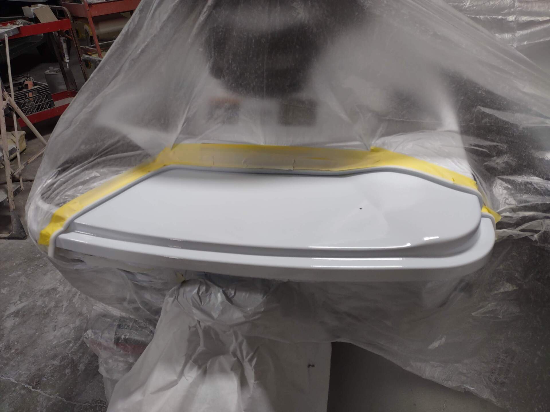White car part masked with plastic and yellow tape in a workshop