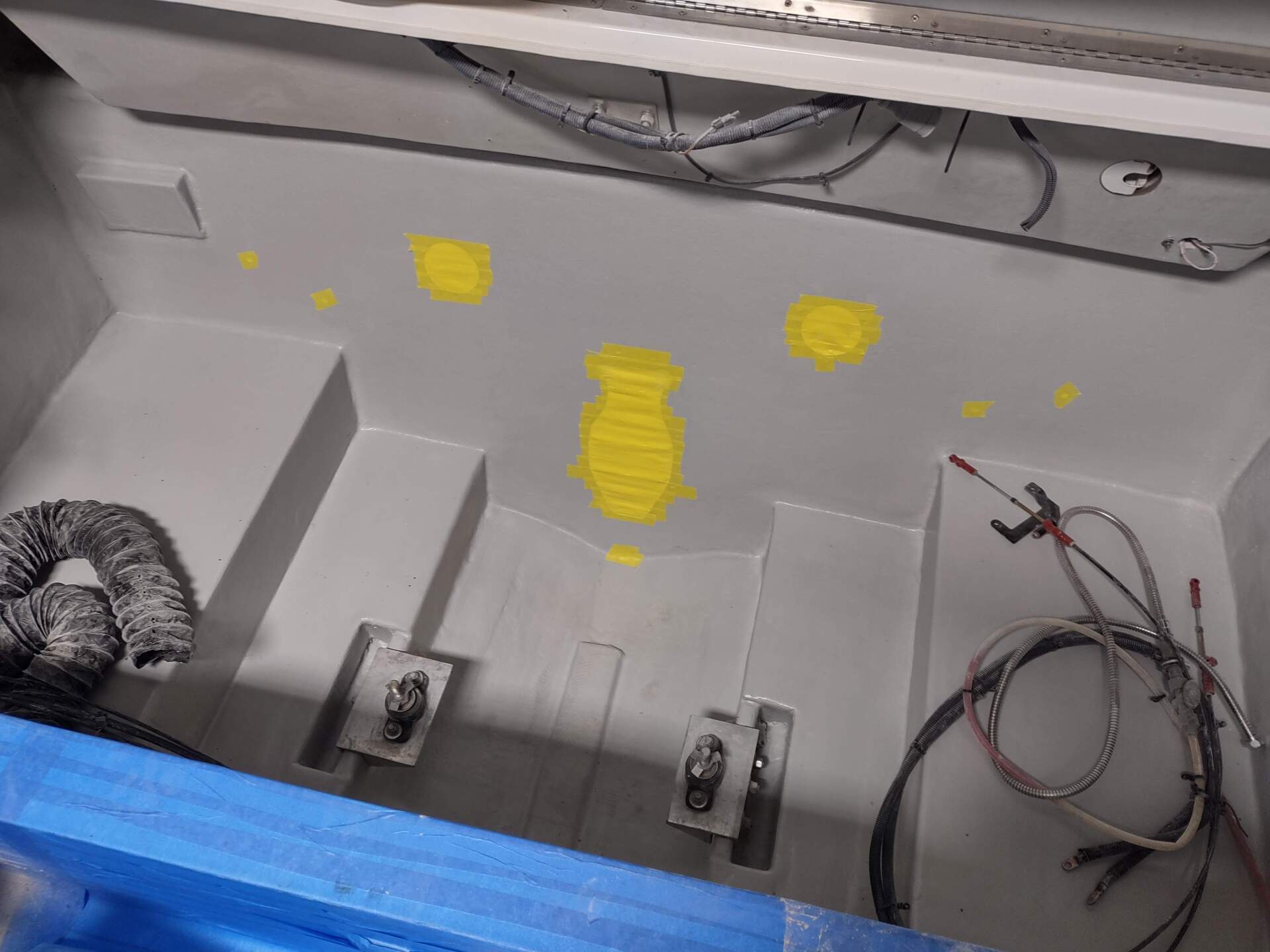Gray metal compartment with wiring, mounted parts, and yellow paint marks along the top edge