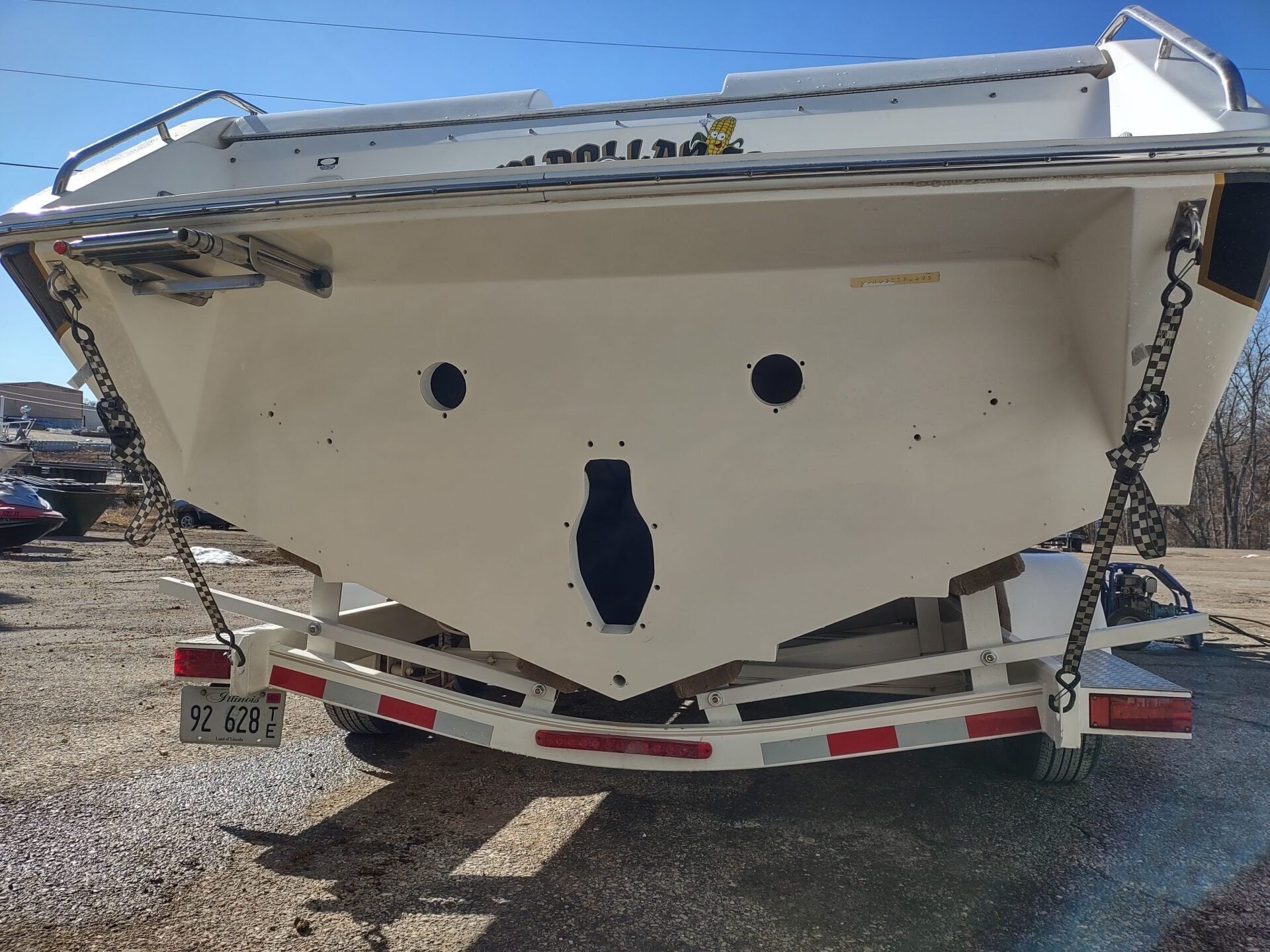 White boat stern on a trailer, viewed from behind in a gravel lot