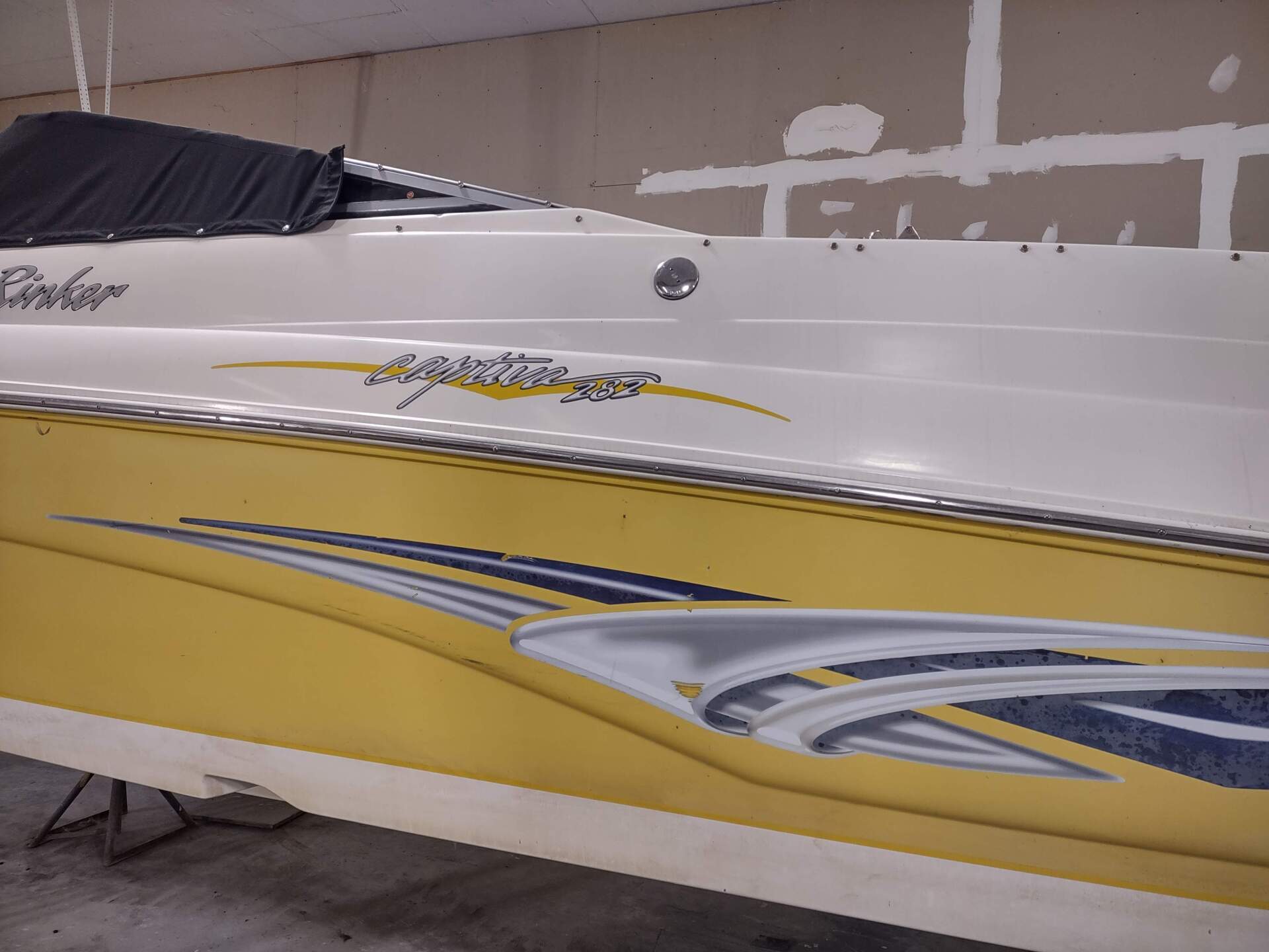 Yellow and white speedboat hull with gray striping, shown indoors in a workshop or garage