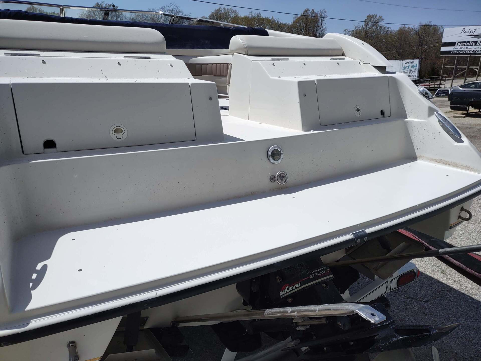 White boat stern with storage compartments and a swim platform in a parking lot