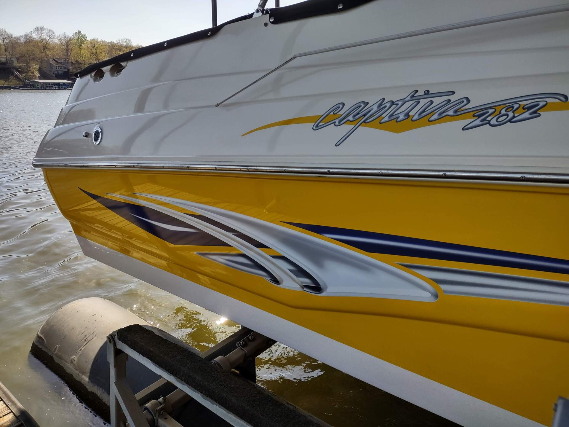 Yellow speedboat hull with silver decals riding on a trailer near the water