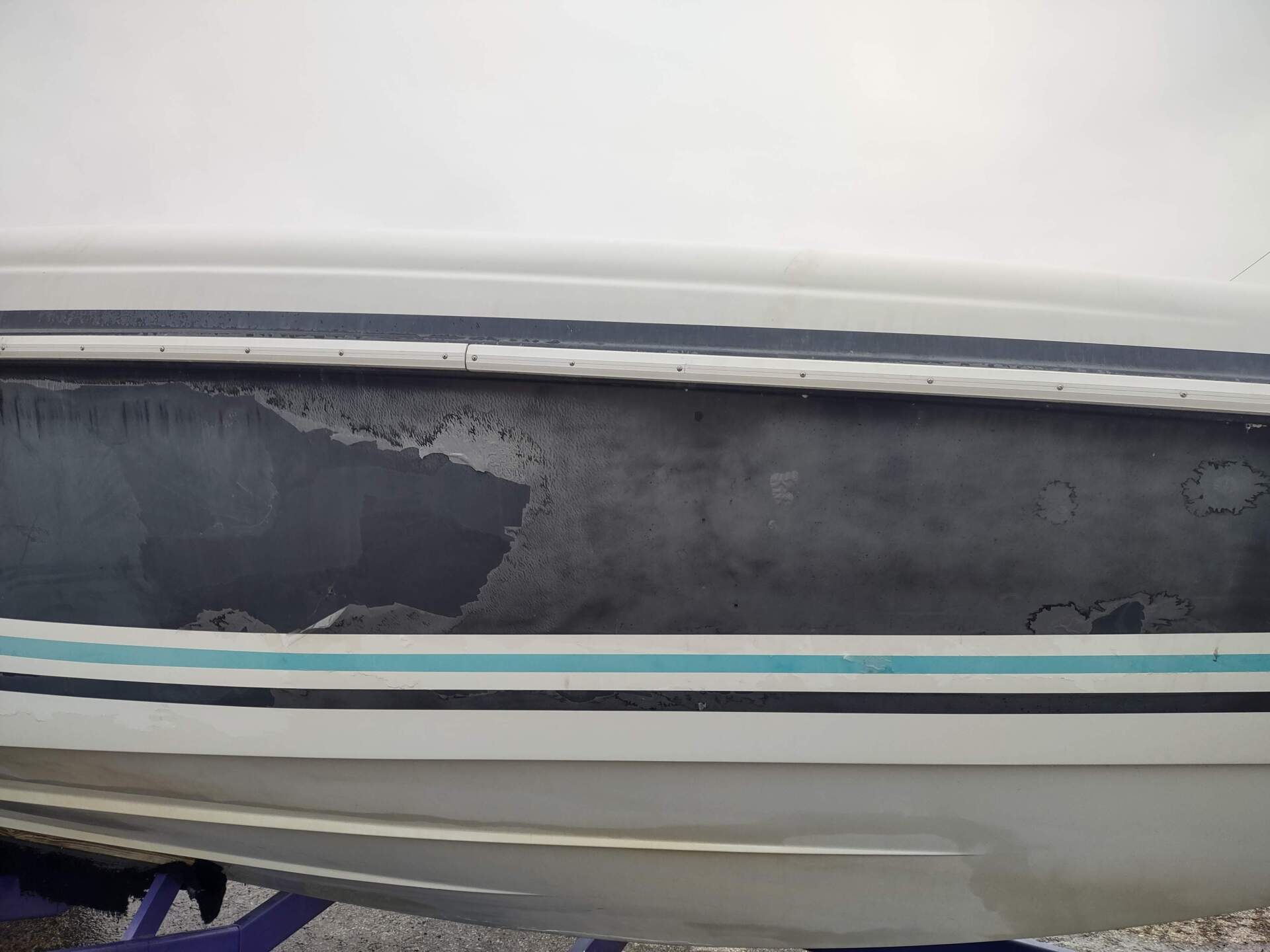 Side view of a small white boat with a gray tarp and teal stripe, showing a weathered patch on the hull