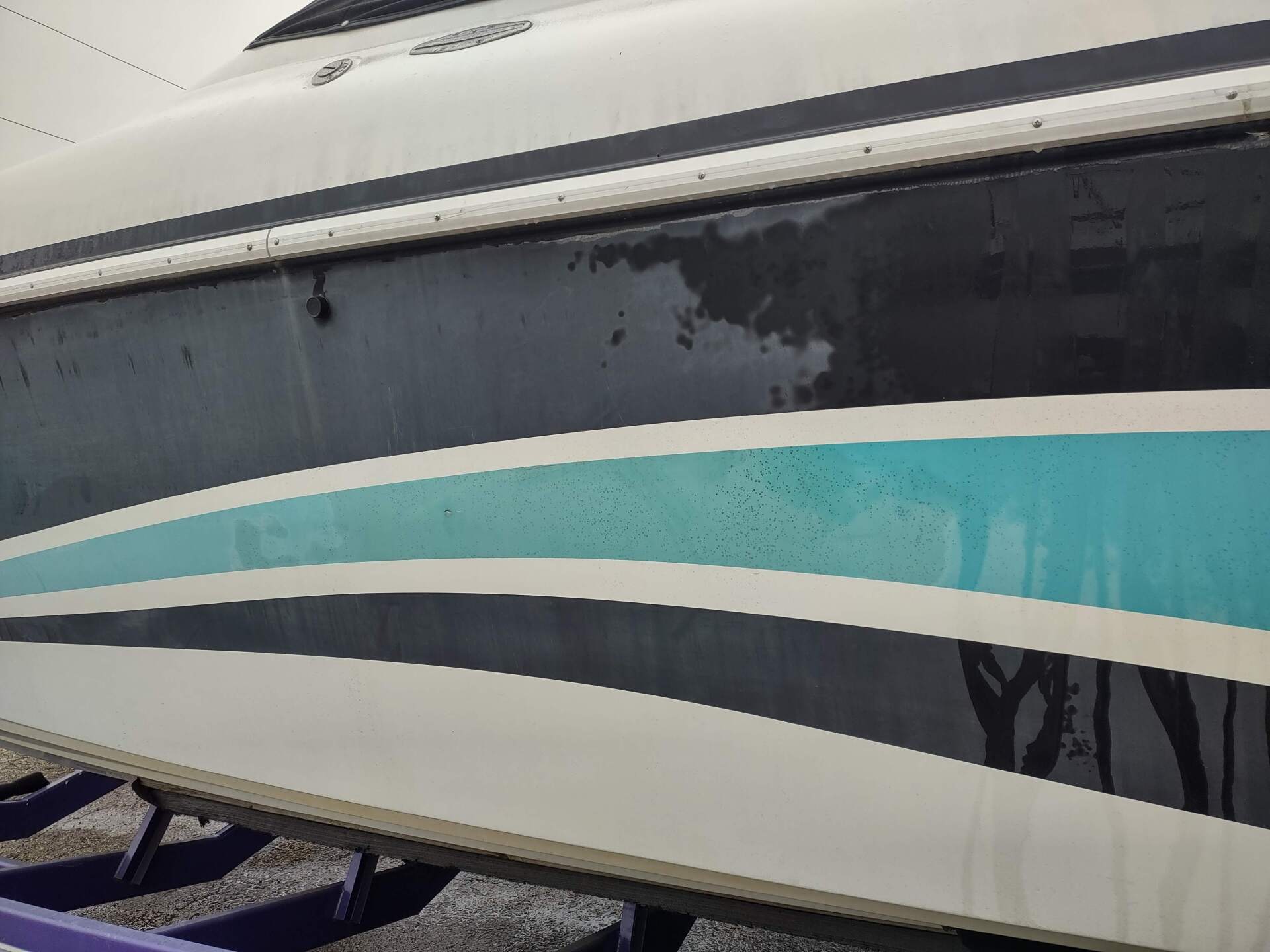 Close-up of a boat hull with teal and black stripes on a white background