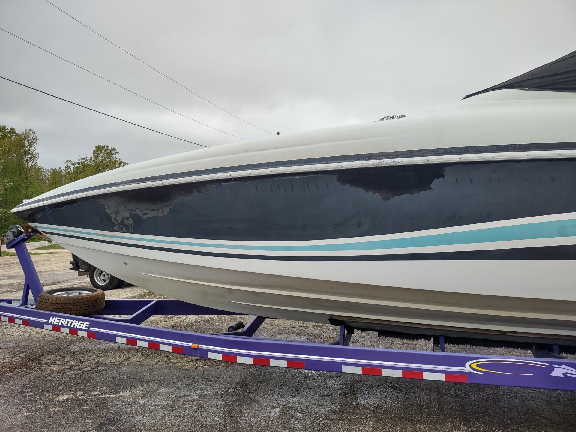 White speedboat on a purple trailer, with blue and black striping, parked outdoors under cloudy skies