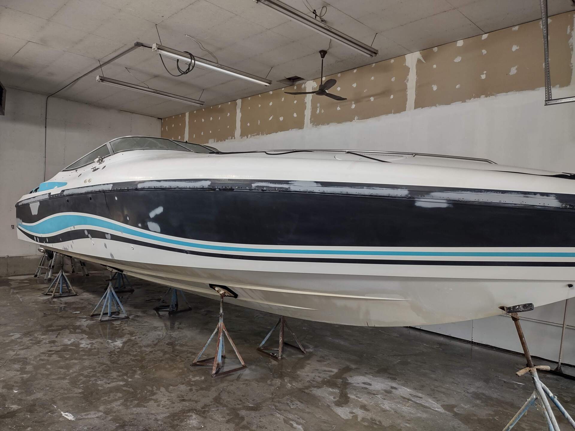 Large white and navy speedboat on stands inside a warehouse, with blue and black stripes.