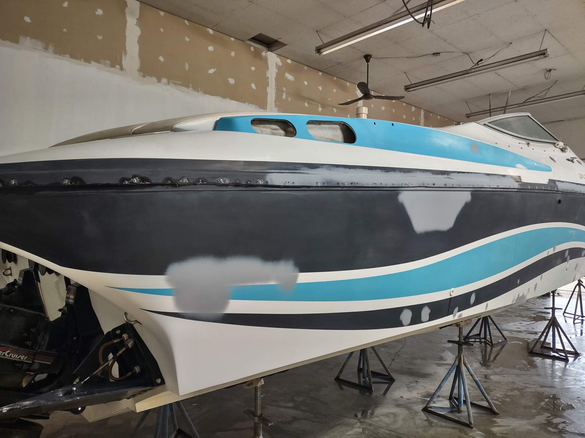 Large white, black, and turquoise boat on stands inside a boatyard workshop