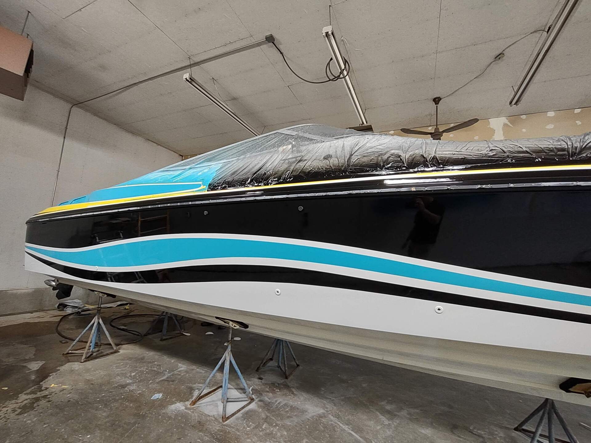Black-and-teal speedboat on stands inside a garage, with a dusting of snow on top.