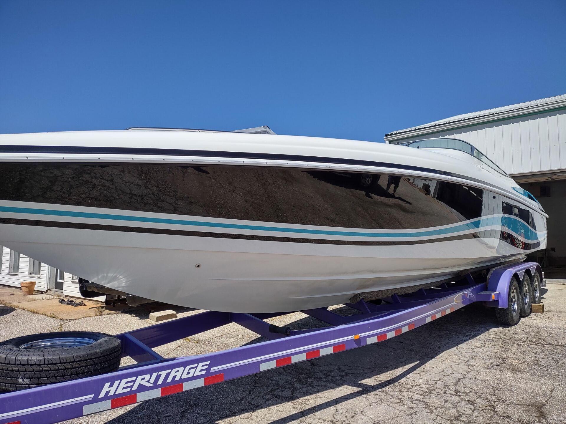 White speedboat on a purple trailer in a gravel lot under a clear blue sky