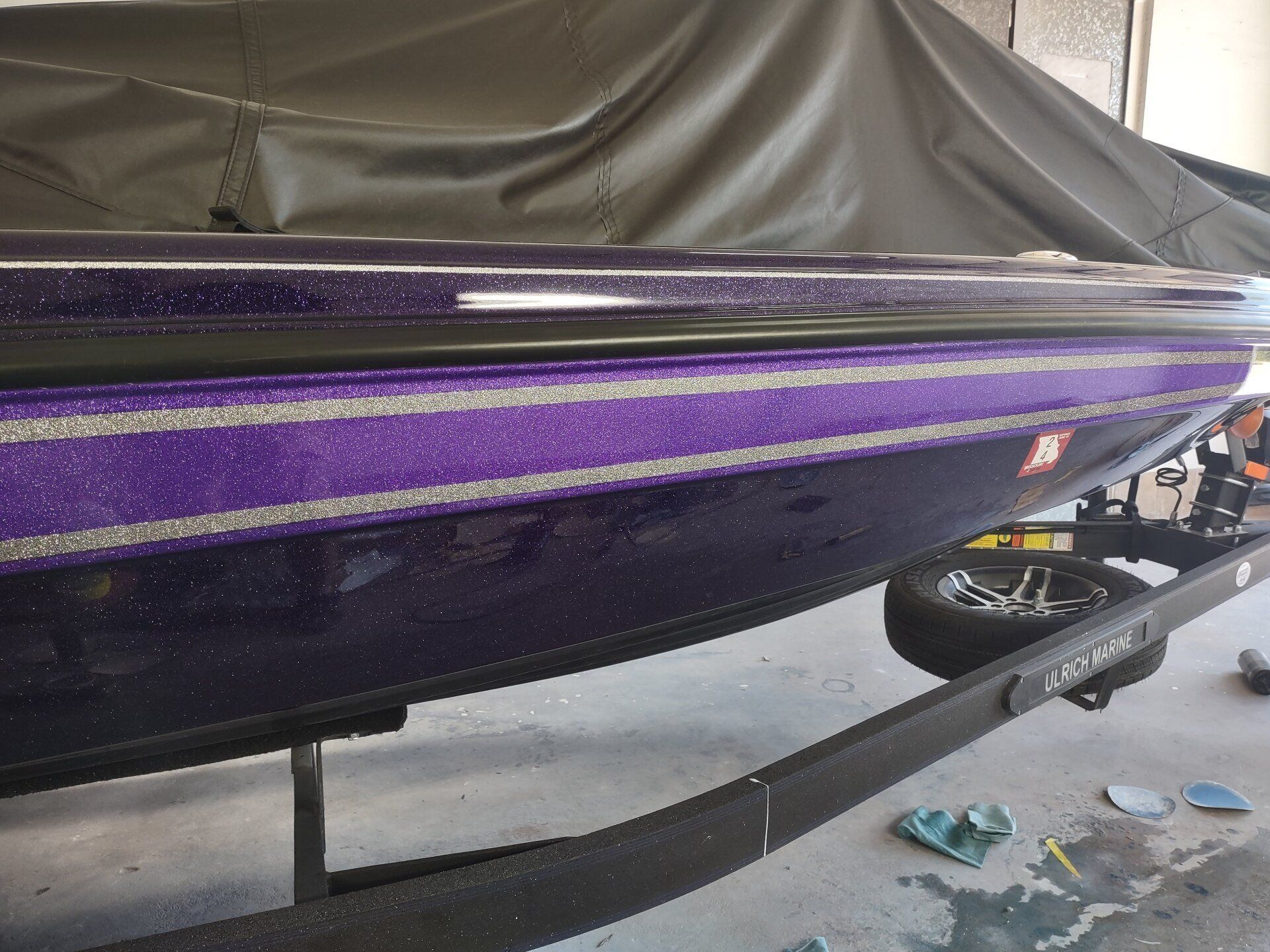 Purple boat hull on a trailer, covered with a gray tarp in a garage.