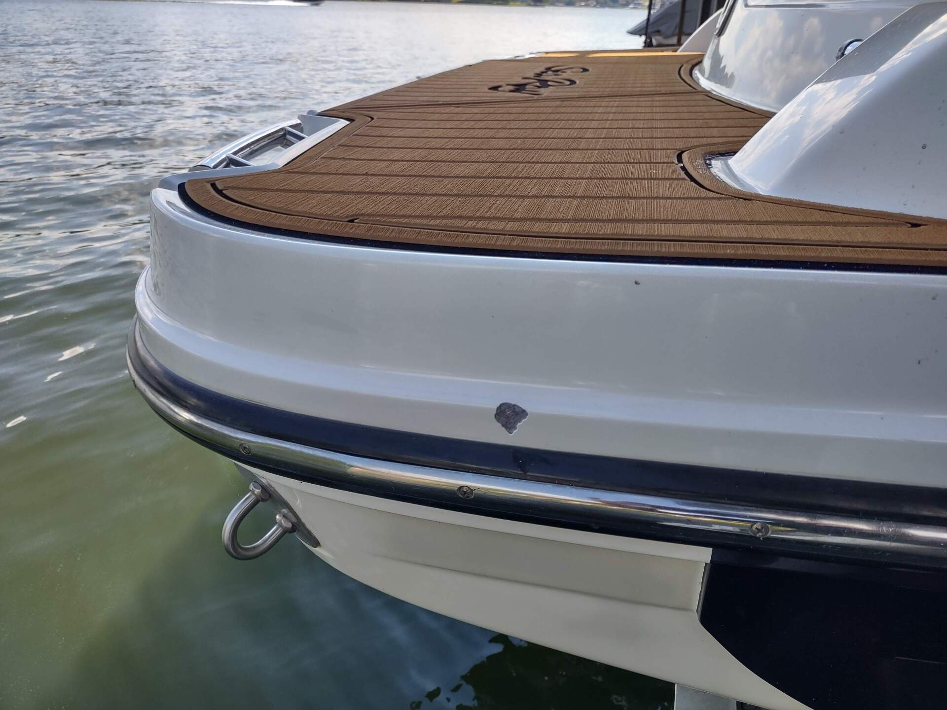 Close-up of a boat’s stern with a teak deck and white hull floating on calm water