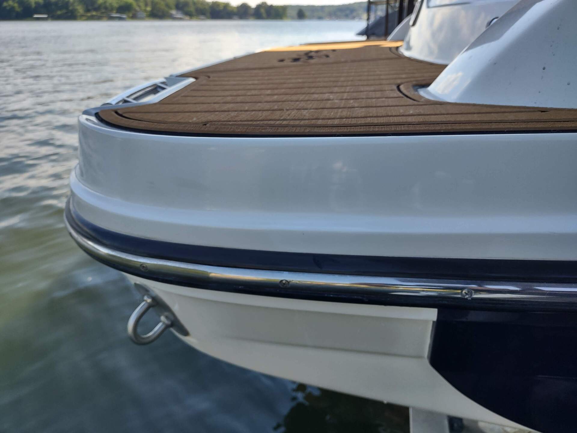 Close-up of a white and blue boat stern with teak deck on calm water