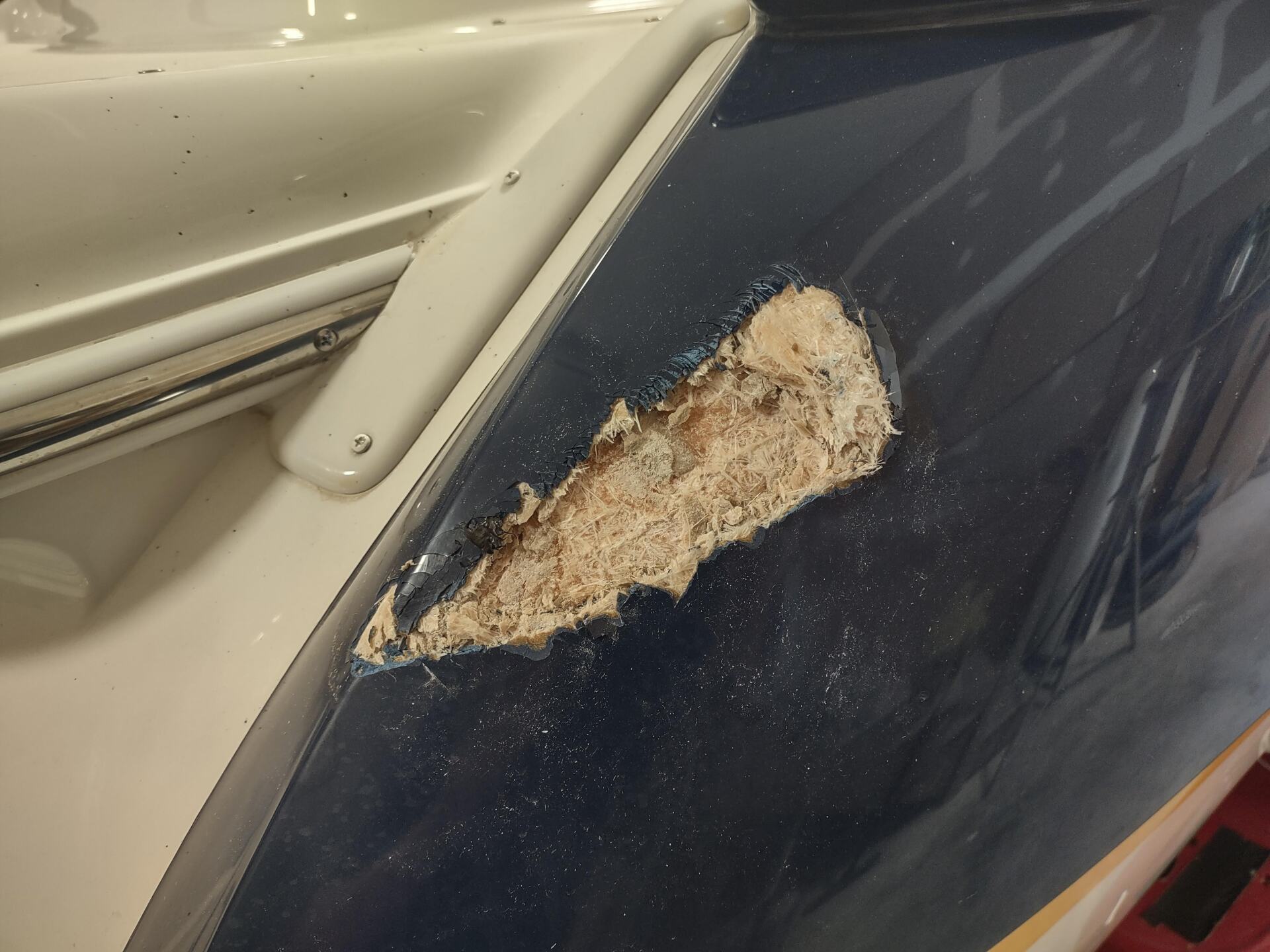 Close-up of a blue car panel with a large chipped paint and rust patch near a beige trim piece
