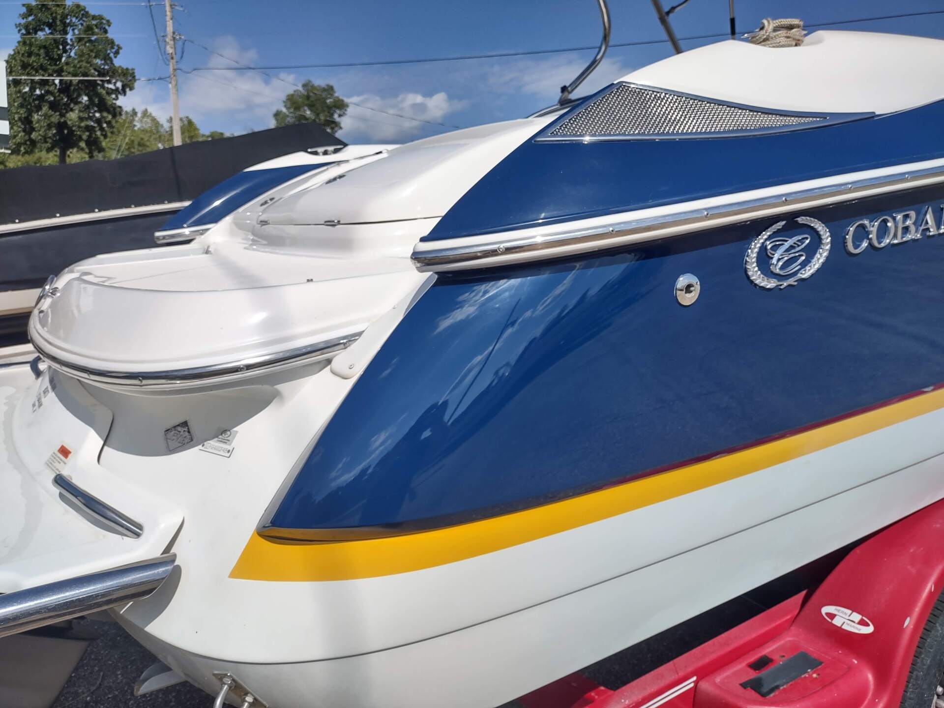 Blue and white speedboat with yellow stripe docked beside a red boat under a sunny sky