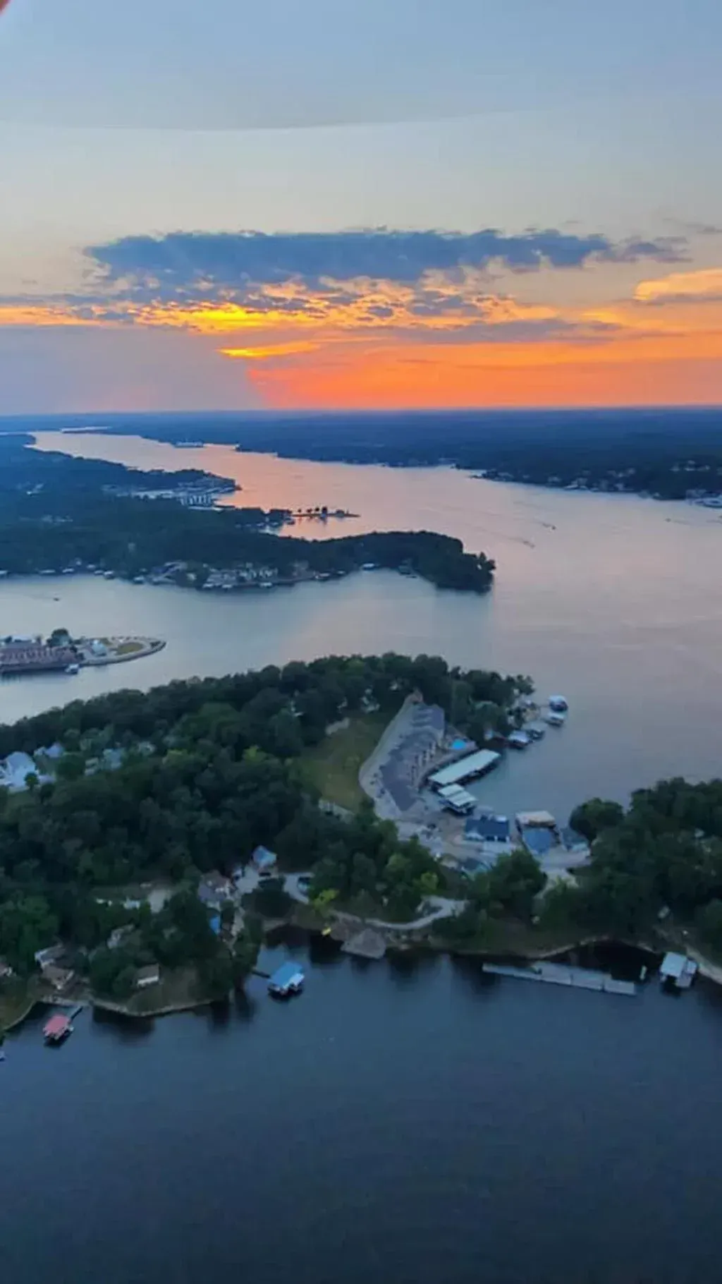 Sunset over a river and wooded shoreline, with islands and boats in calm water.