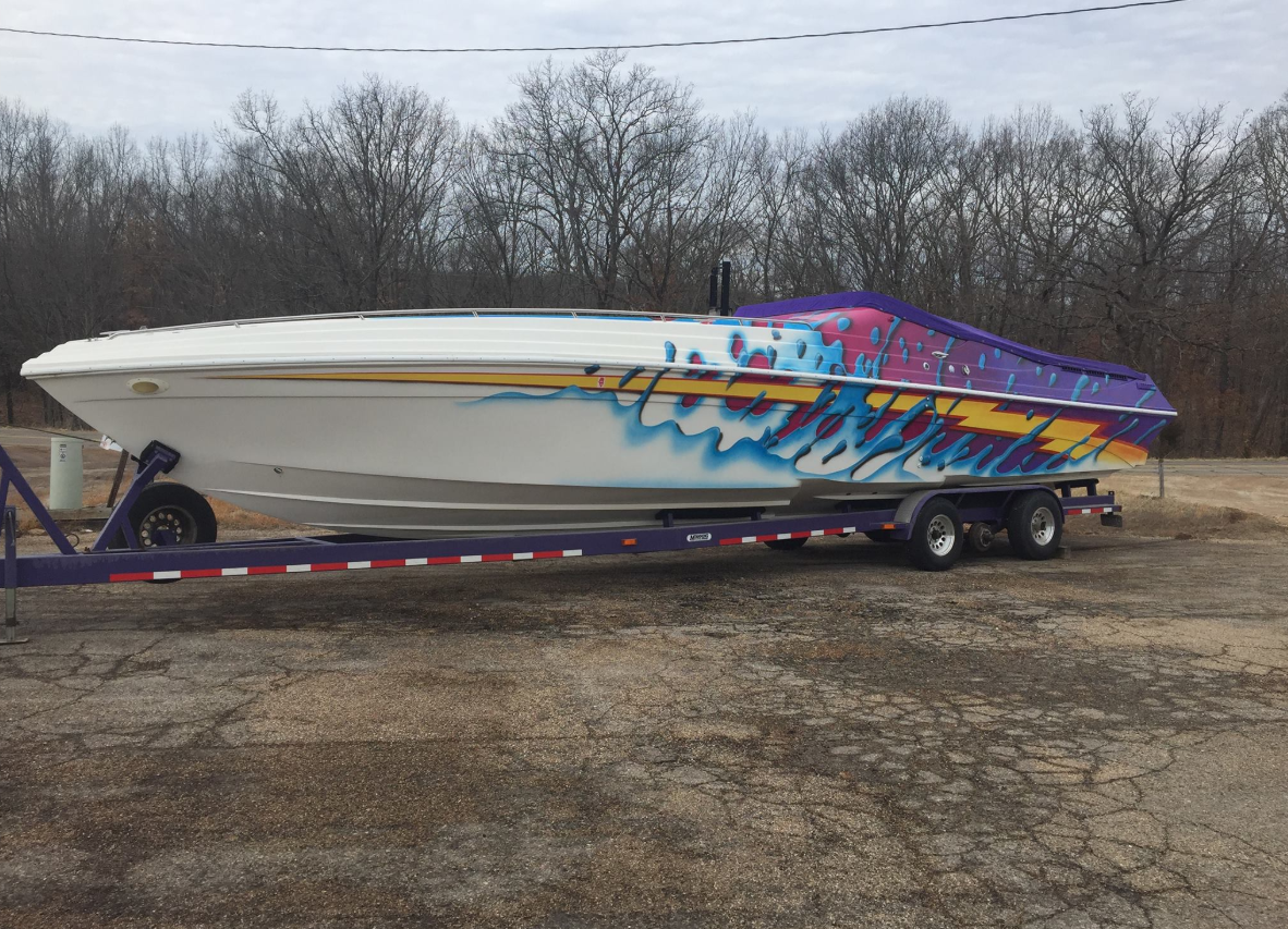 White speedboat with colorful graphics on a trailer in a dirt lot, under an overcast sky.