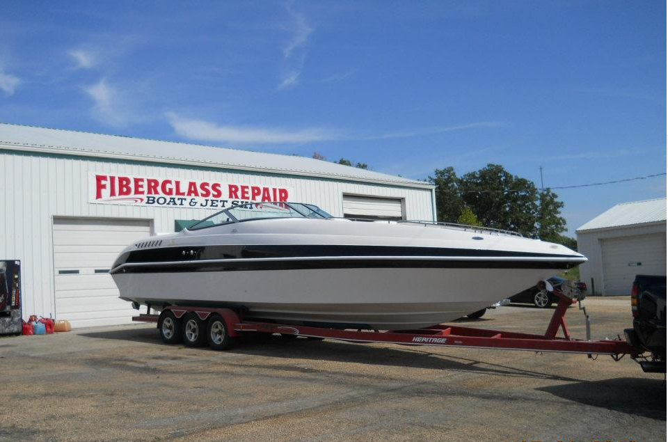 Large white-and-black boat on a trailer outside a fiberglass repair shop under a blue sky