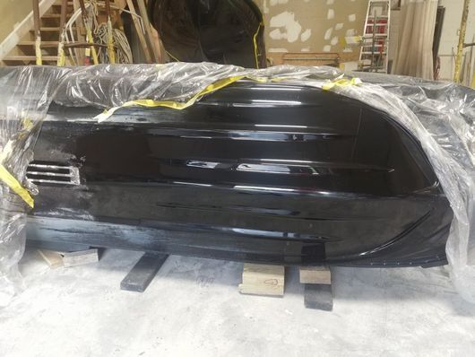 Black glossy kayak or canoe wrapped in plastic, resting on wooden pallets in a warehouse