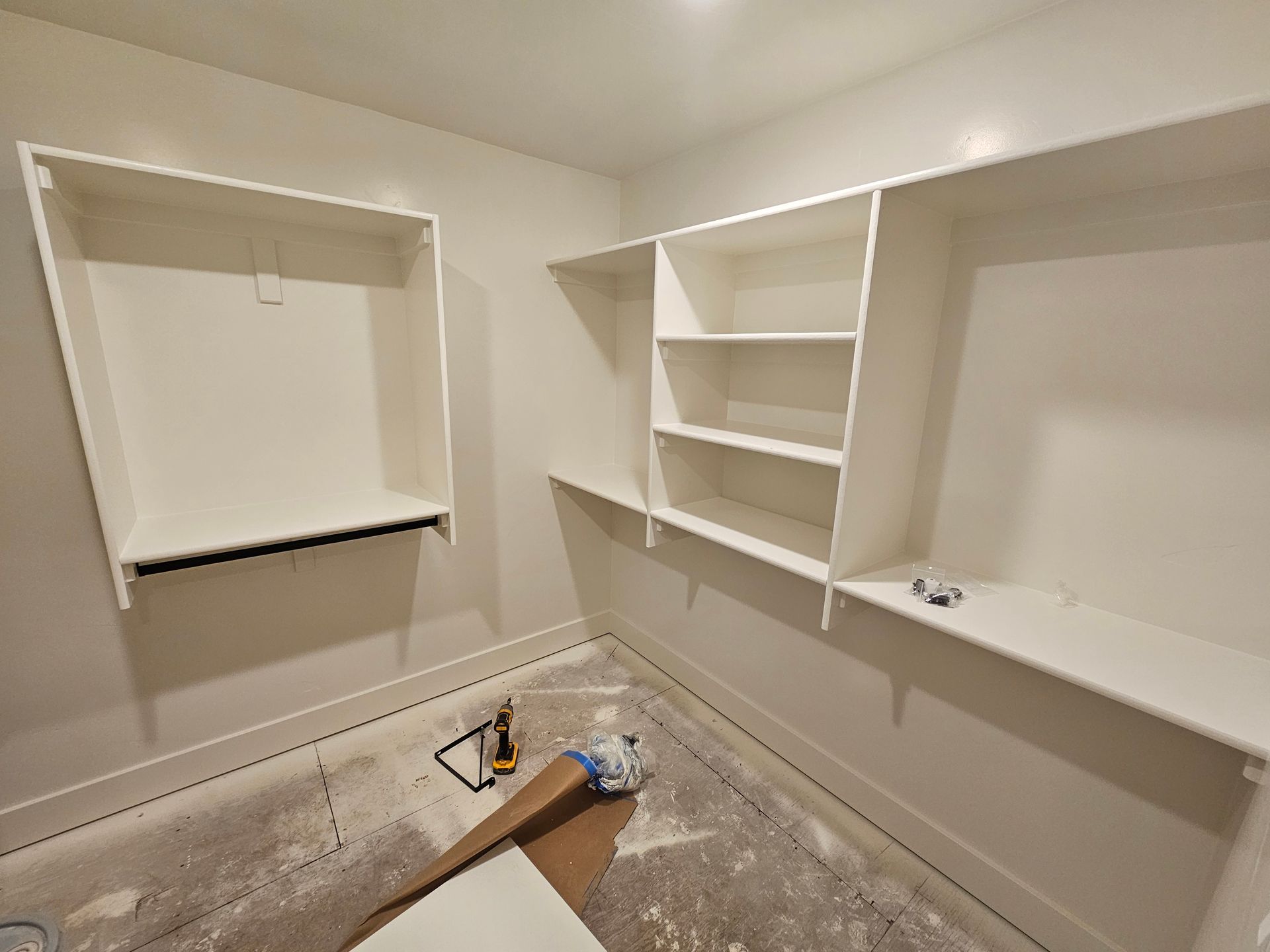 Empty white closet with built-in shelves and a rod for hanging clothes. Construction materials on floor.