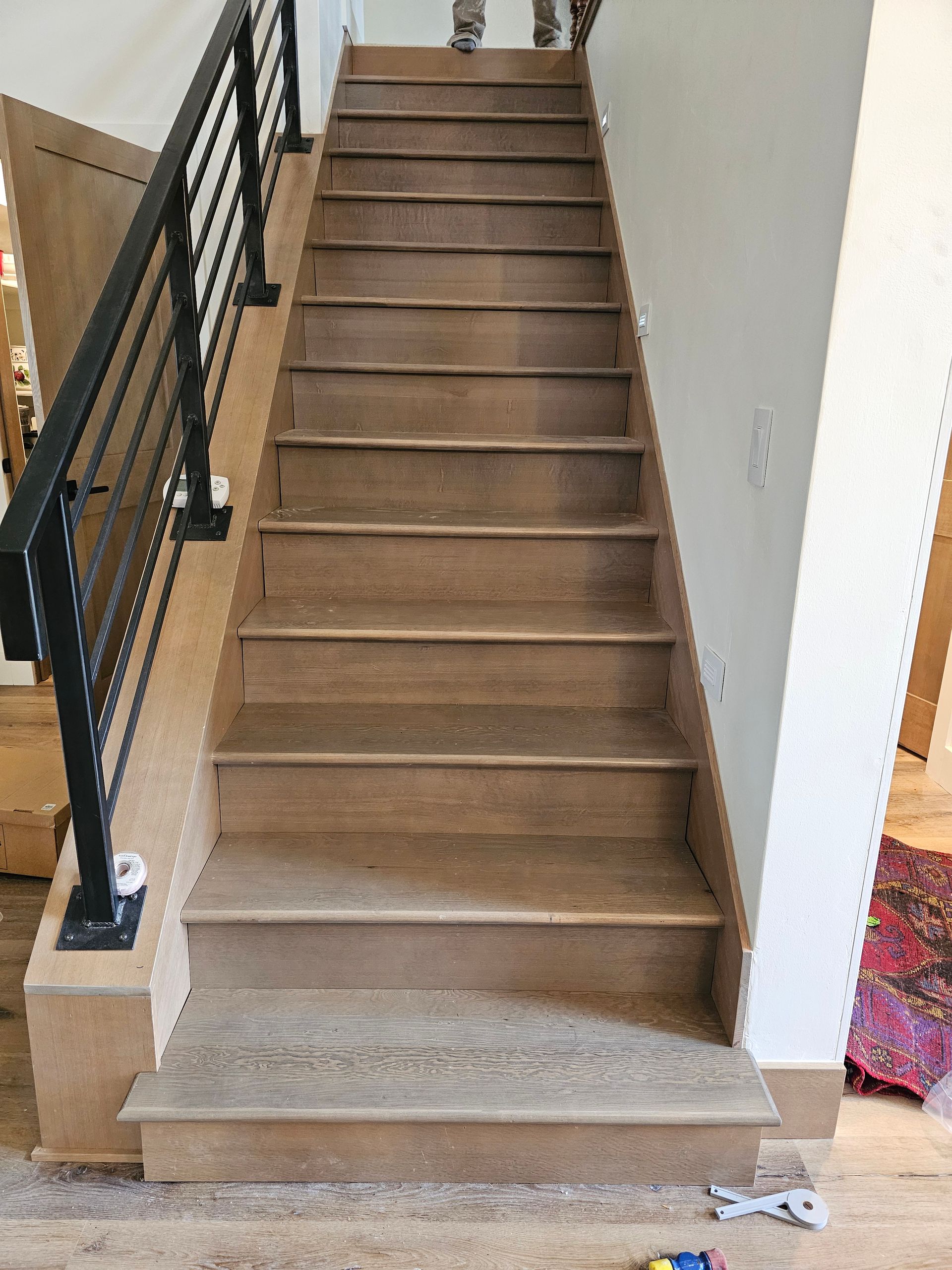 Wooden staircase with black metal railing, leading upwards.