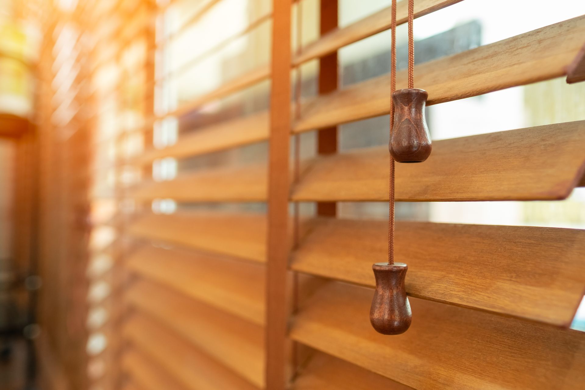 Wooden window blinds, partially open, with pull strings hanging down.