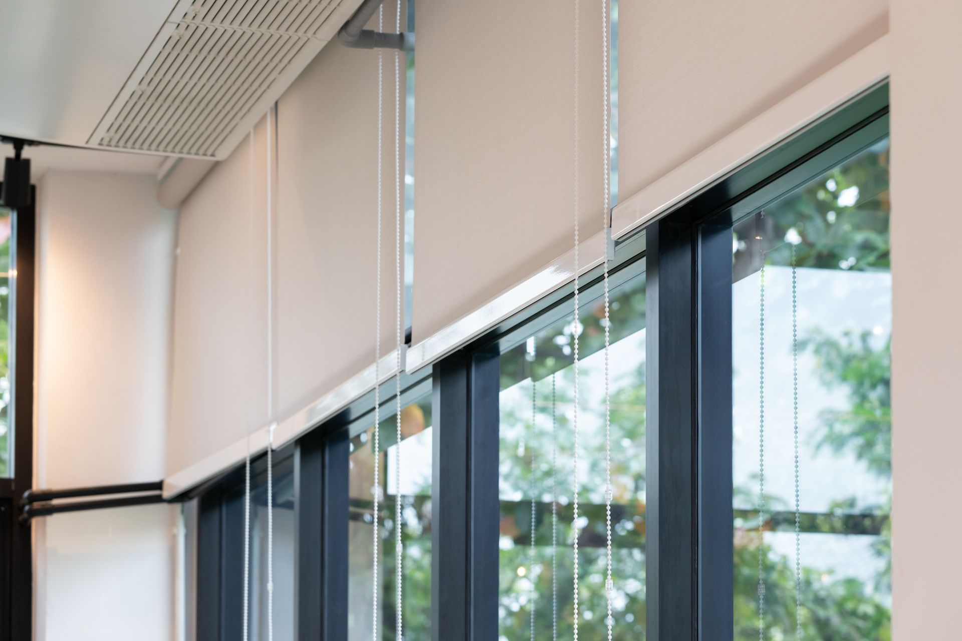 Roller blinds in a modern office, covering large windows with a view of greenery outside.
