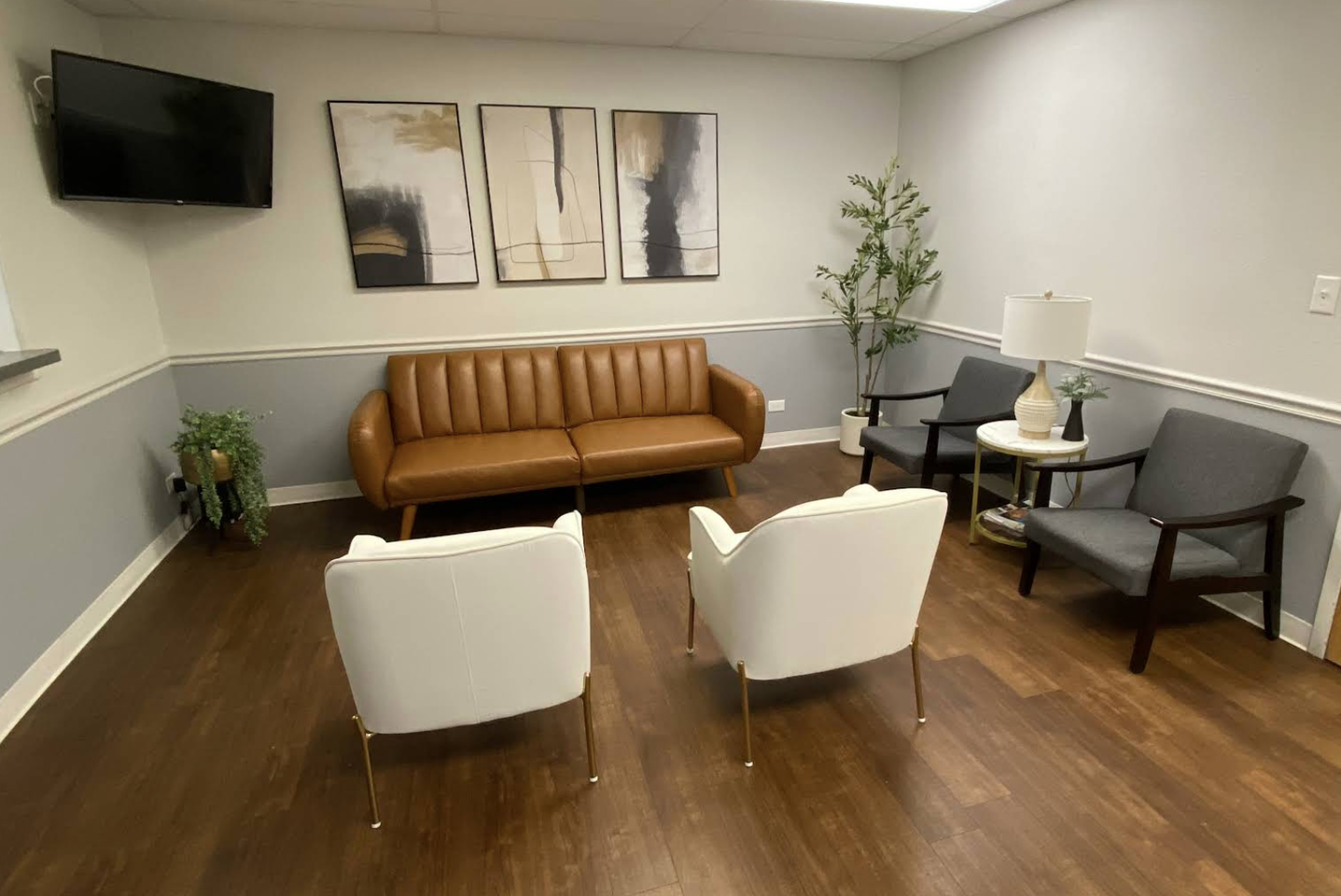 Waiting room with brown leather couch, white chairs, and abstract art.