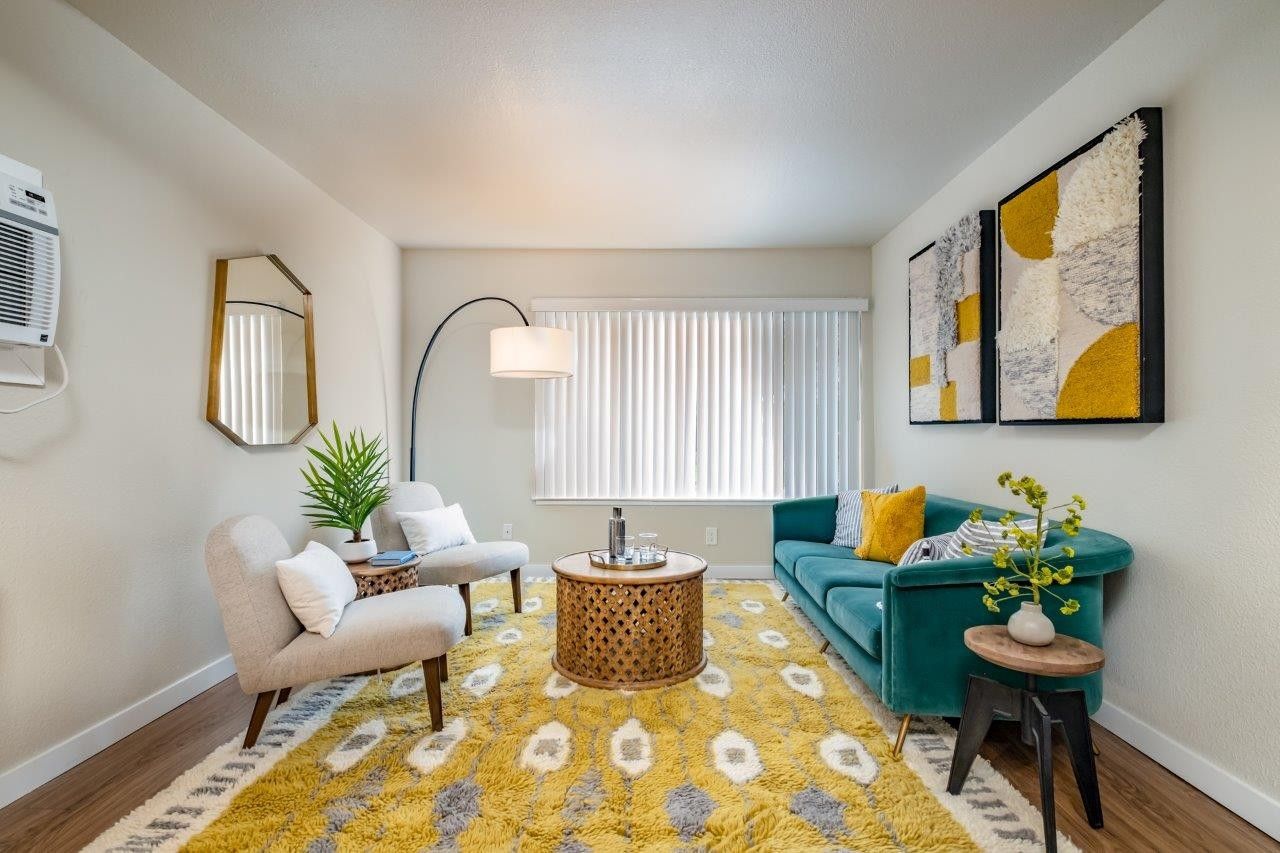 Bright living room with teal sofa, yellow patterned rug, armchair, round table, and abstract wall art