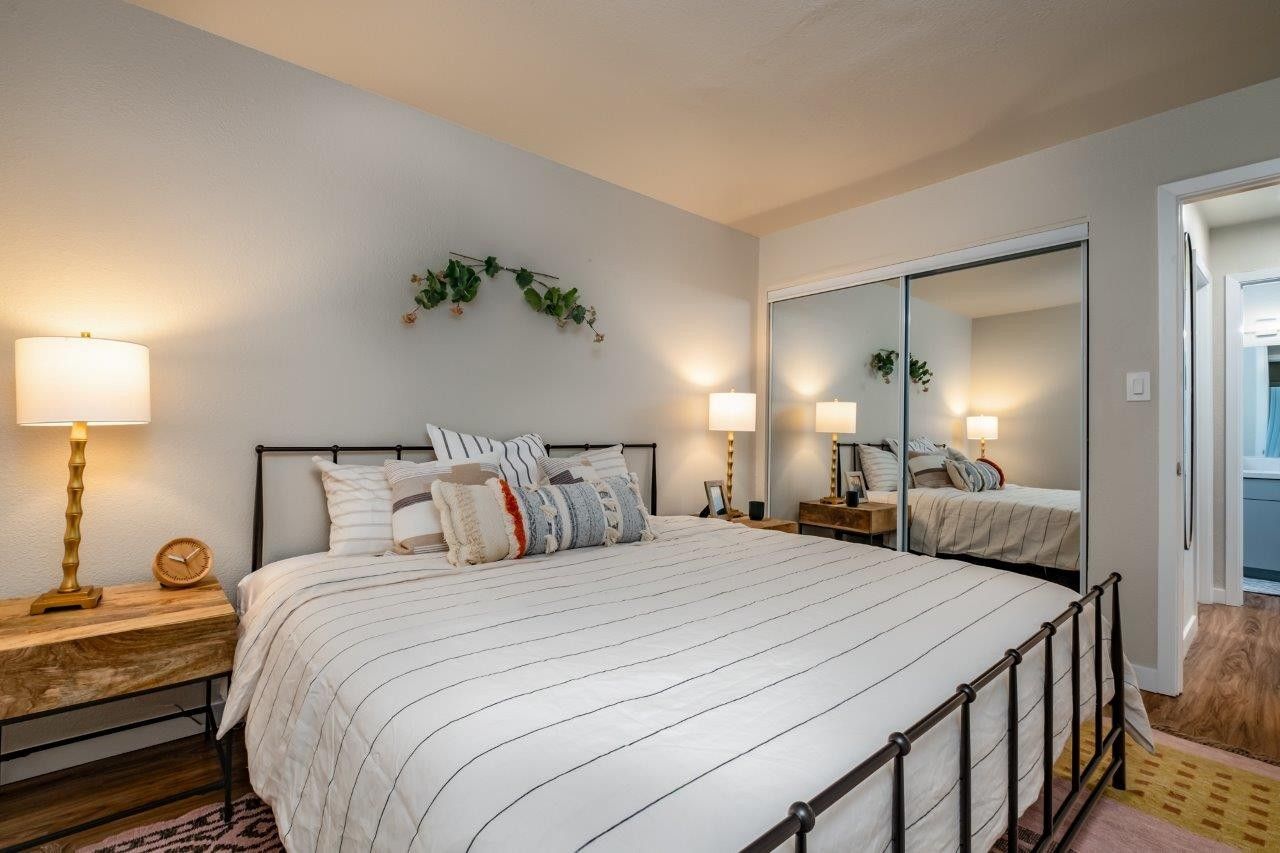 Cozy bedroom with a metal bed, white bedding, nightstands, lamps, and mirrored closet doors