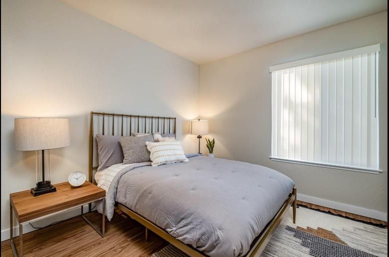 Cozy bedroom with gray bedspread, wooden nightstand, lamp, and window with vertical blinds