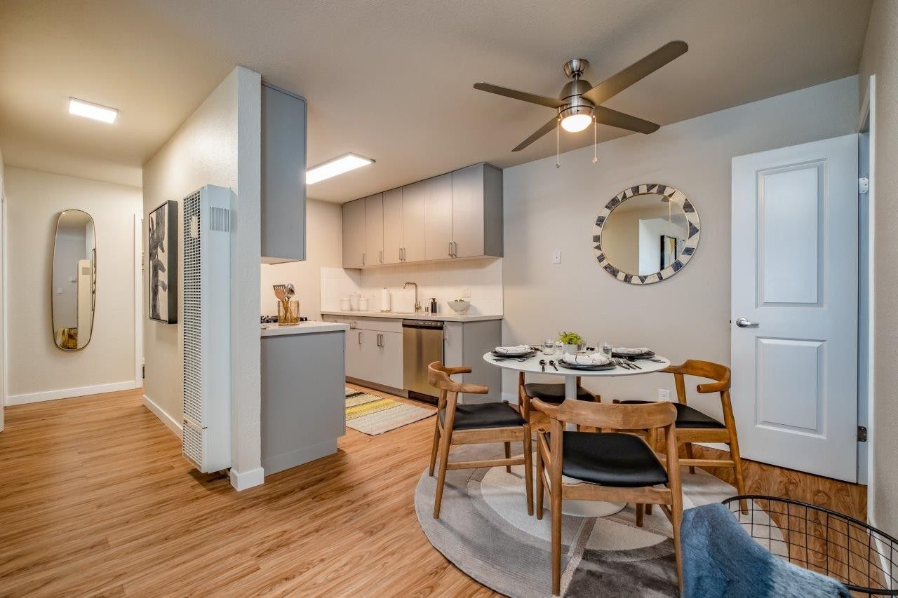 Open-concept apartment dining and kitchen area with wood floors, white cabinets, and ceiling fan