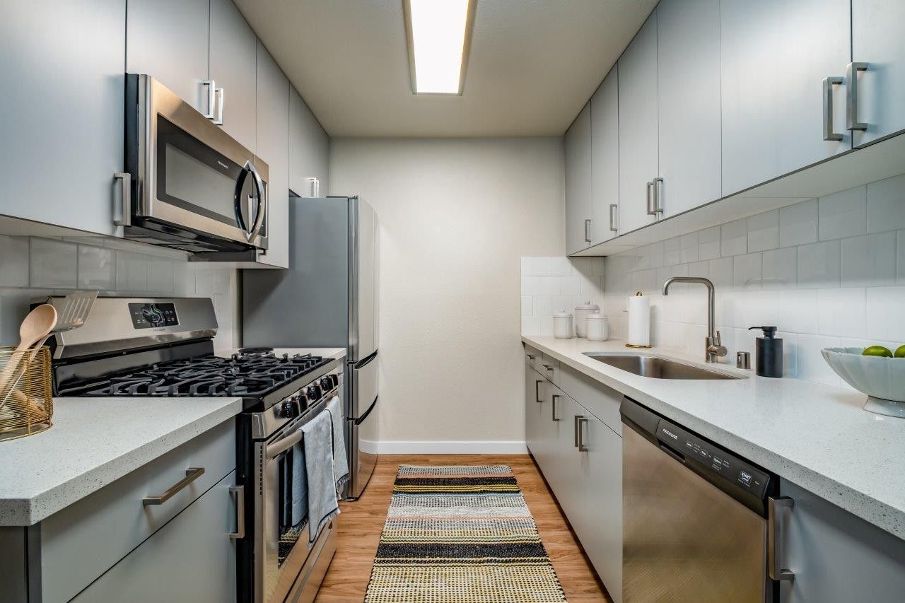 Modern narrow kitchen with stainless steel appliances, white cabinets, and a striped runner rug.