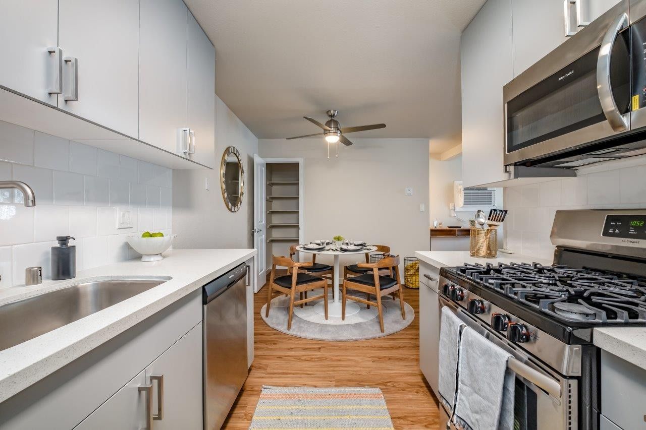 Modern kitchen with white cabinets, stainless appliances, and a small dining table by a window.