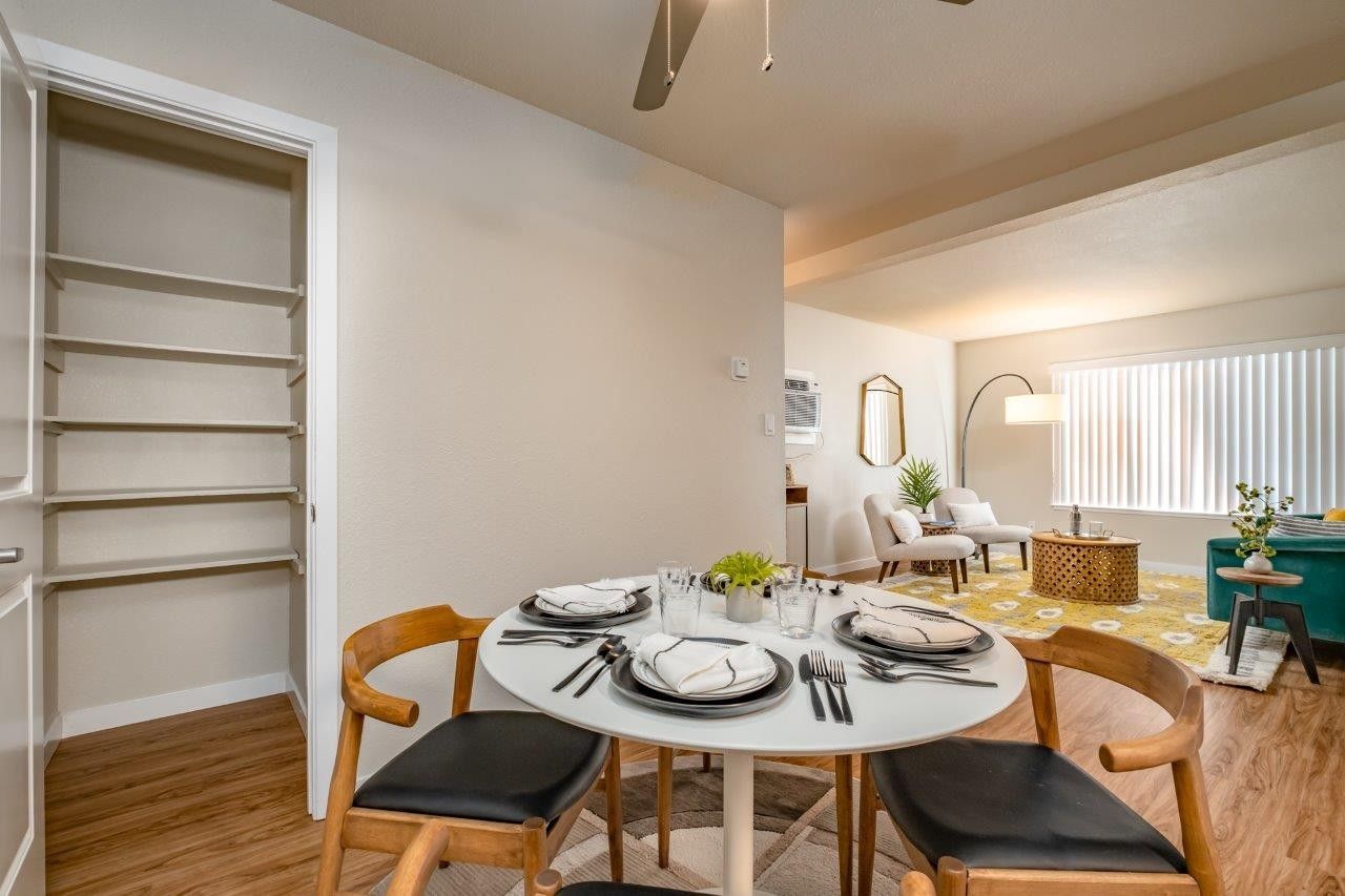 Dining room with round white table, black chairs, and open shelving in a bright adjoining living area