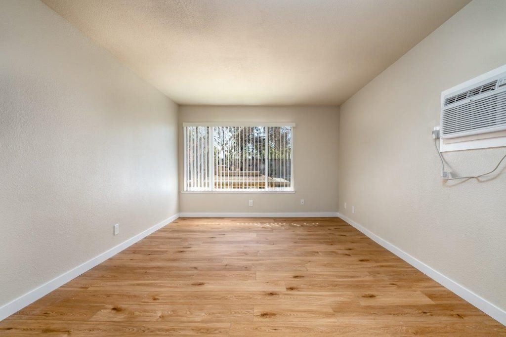 Empty room with hardwood floor, white walls, and a window with vertical blinds.